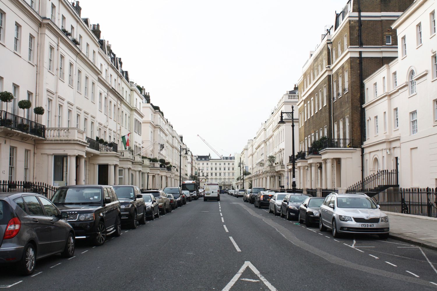 A view down the middle of a carriageway on a street of terraced housing.