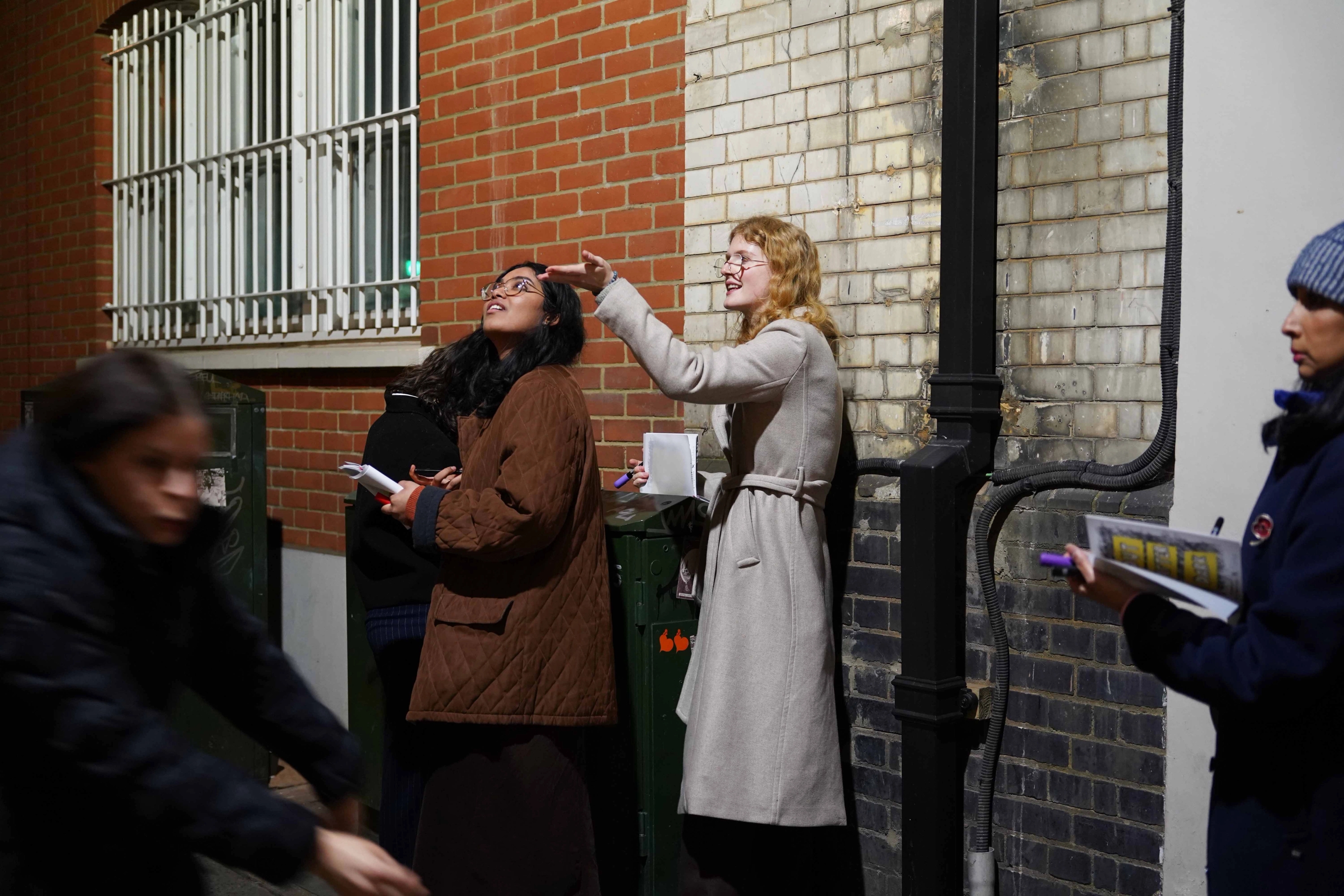 Two people leaning back in front of a brick wall and looking up as one points.