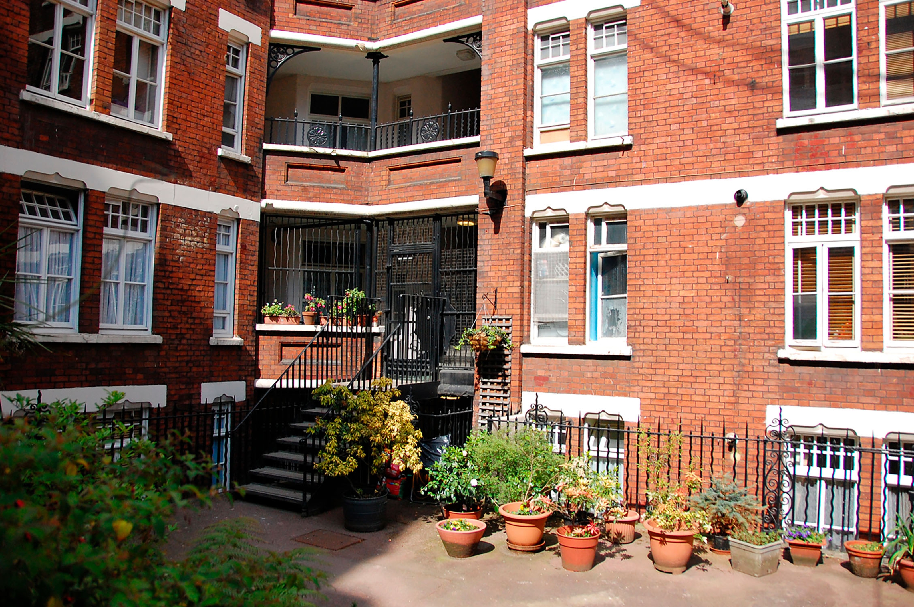 A view of the front steps to a red brick building with plants in terracotta pots.