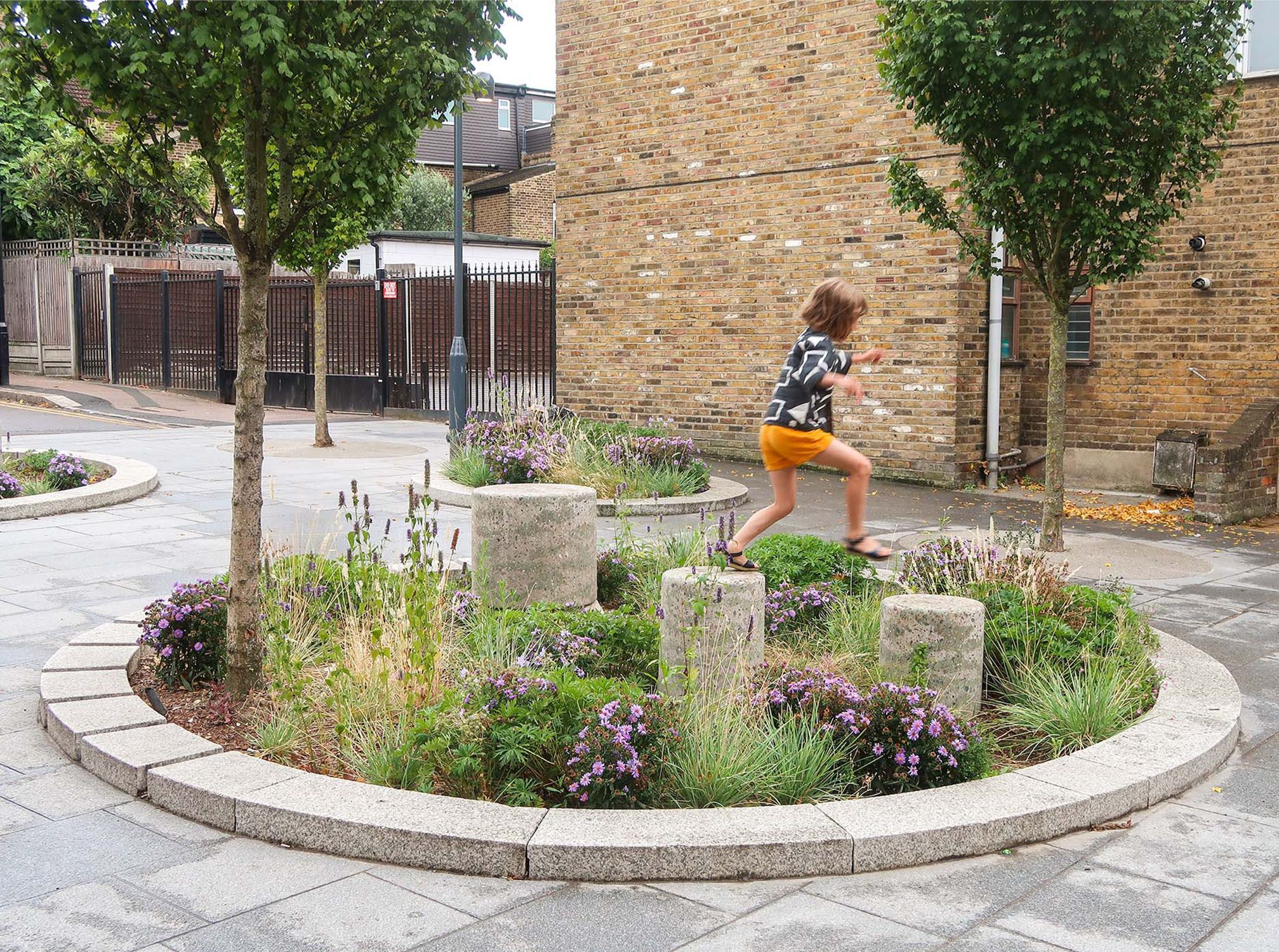Child jumping on stone structures in circular planting bed.