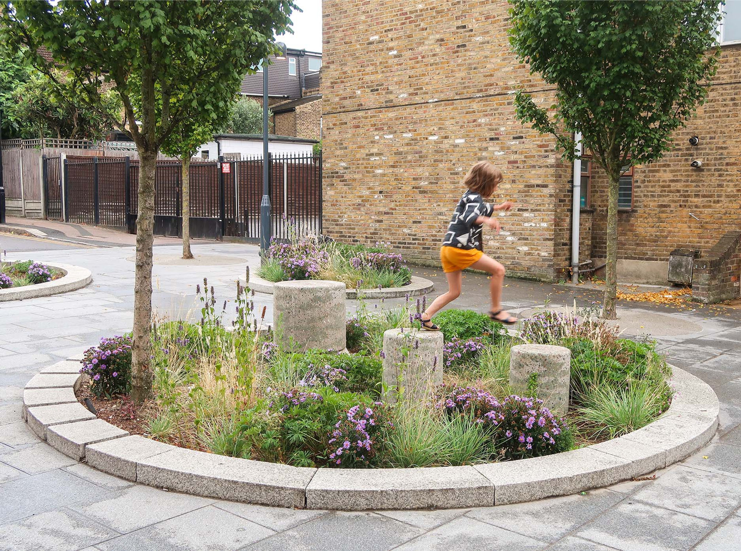 Child jumping on stone structures in circular planting bed.