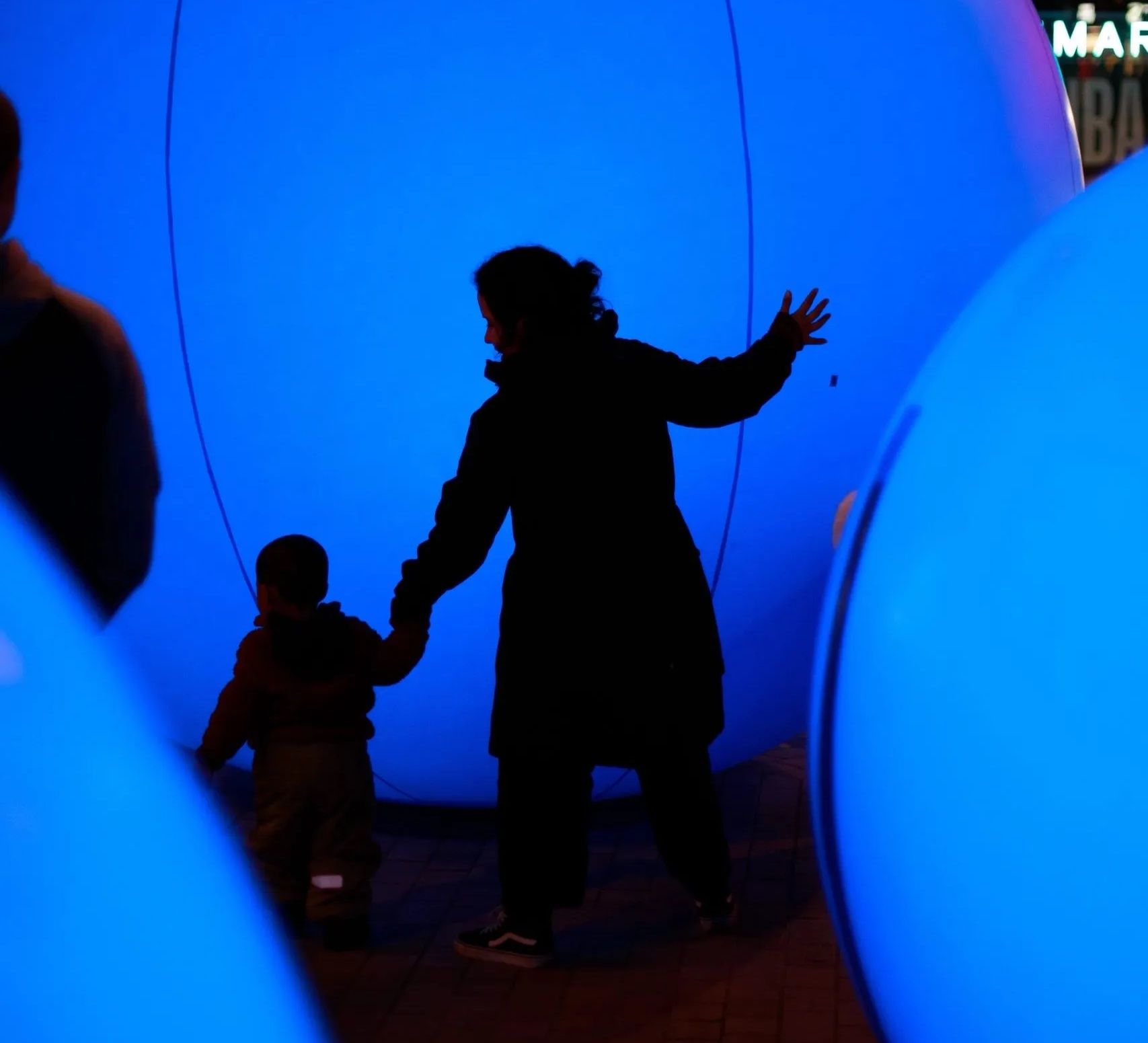 An adult and a child walk between three large illuminated inflated blue orbs.