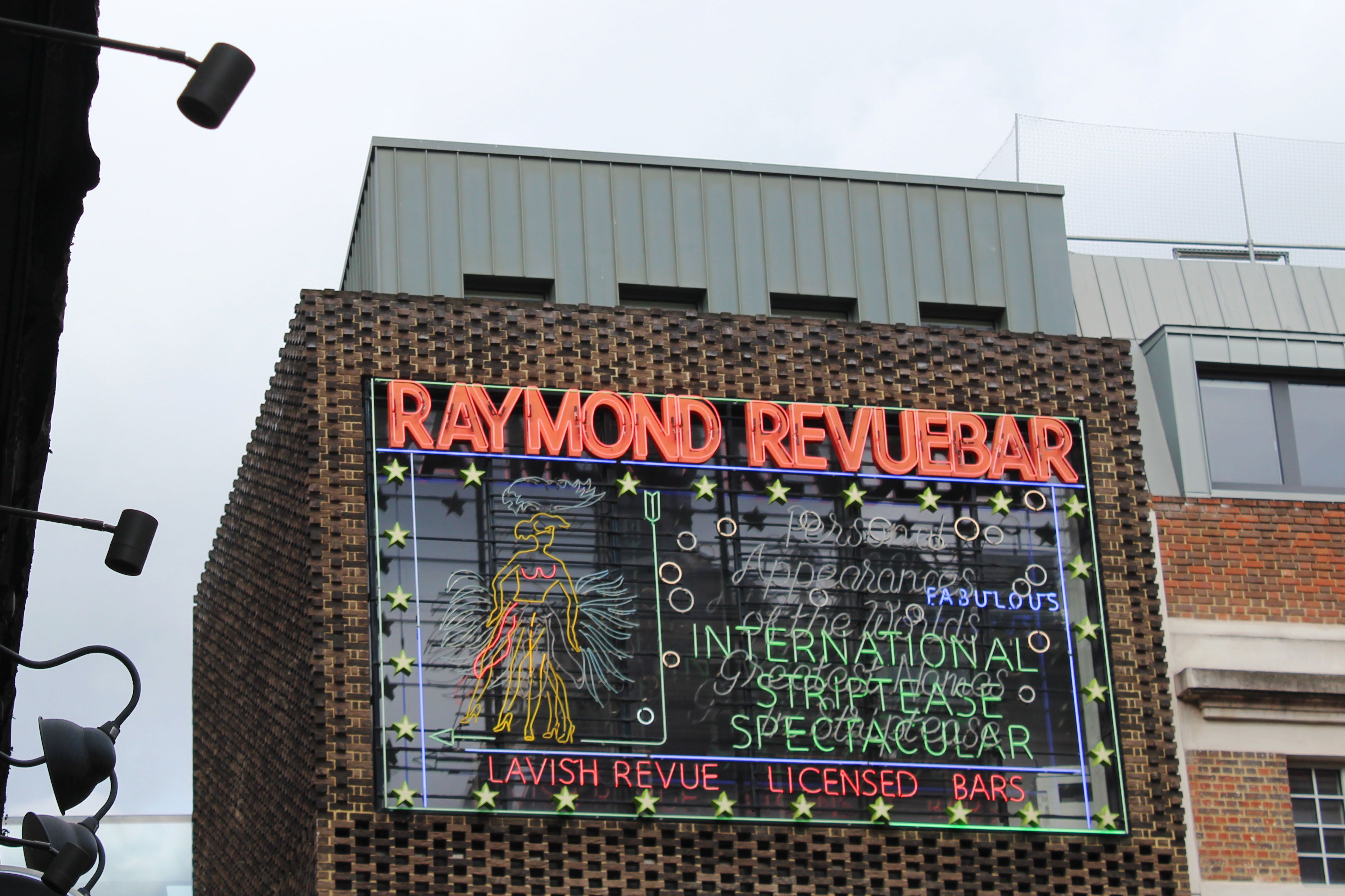 Neon sign on a building reading "RAYMOND REVUEBAR", with an illuminated image of a dancing woman.