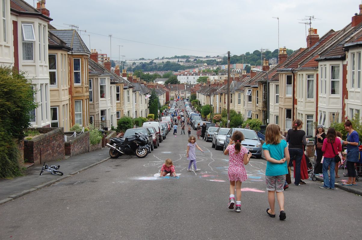 A long street closed to traffic with children playing and drawing on the carriageway.