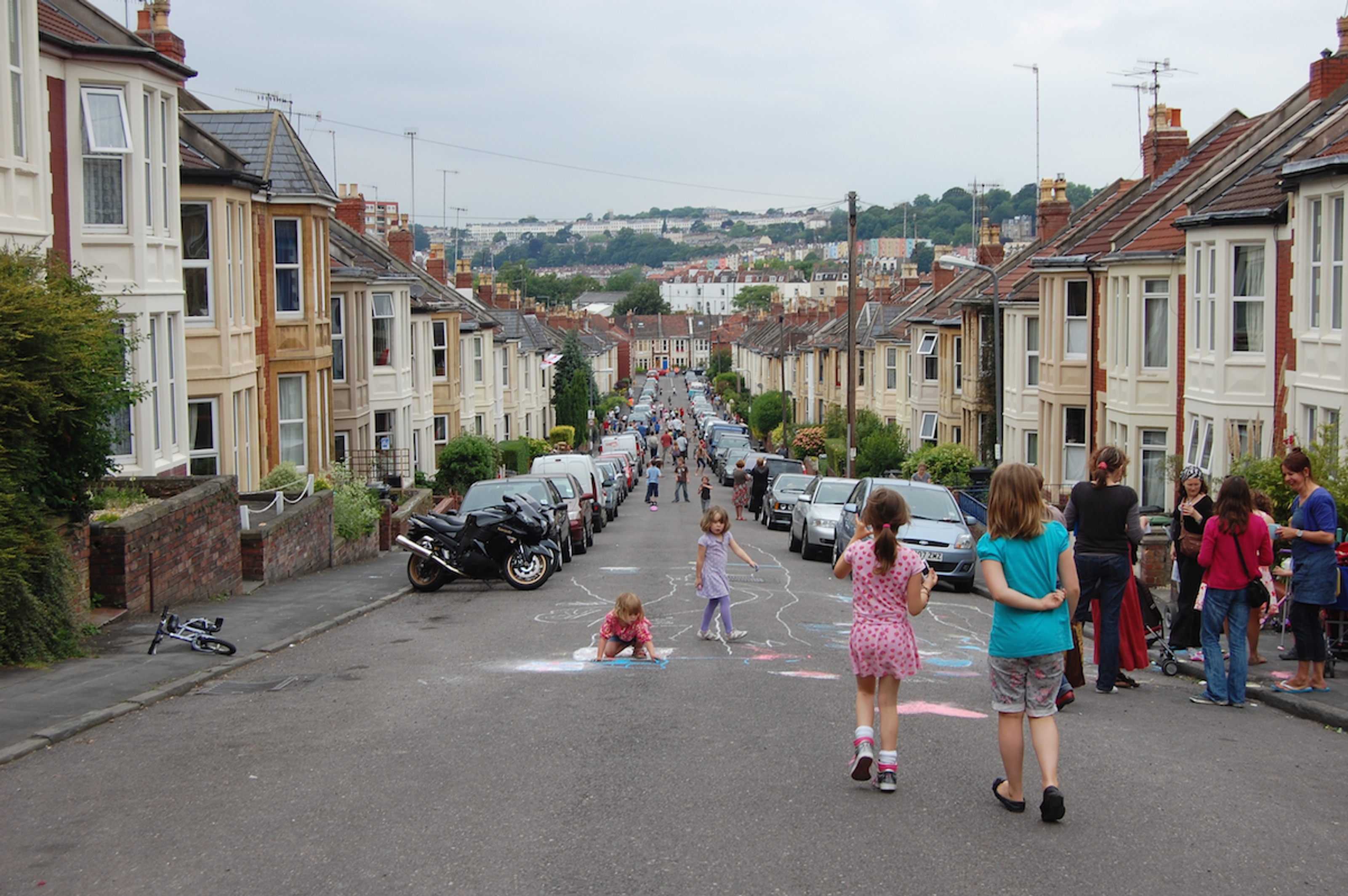 A long street closed to traffic with children playing and drawing on the carriageway.