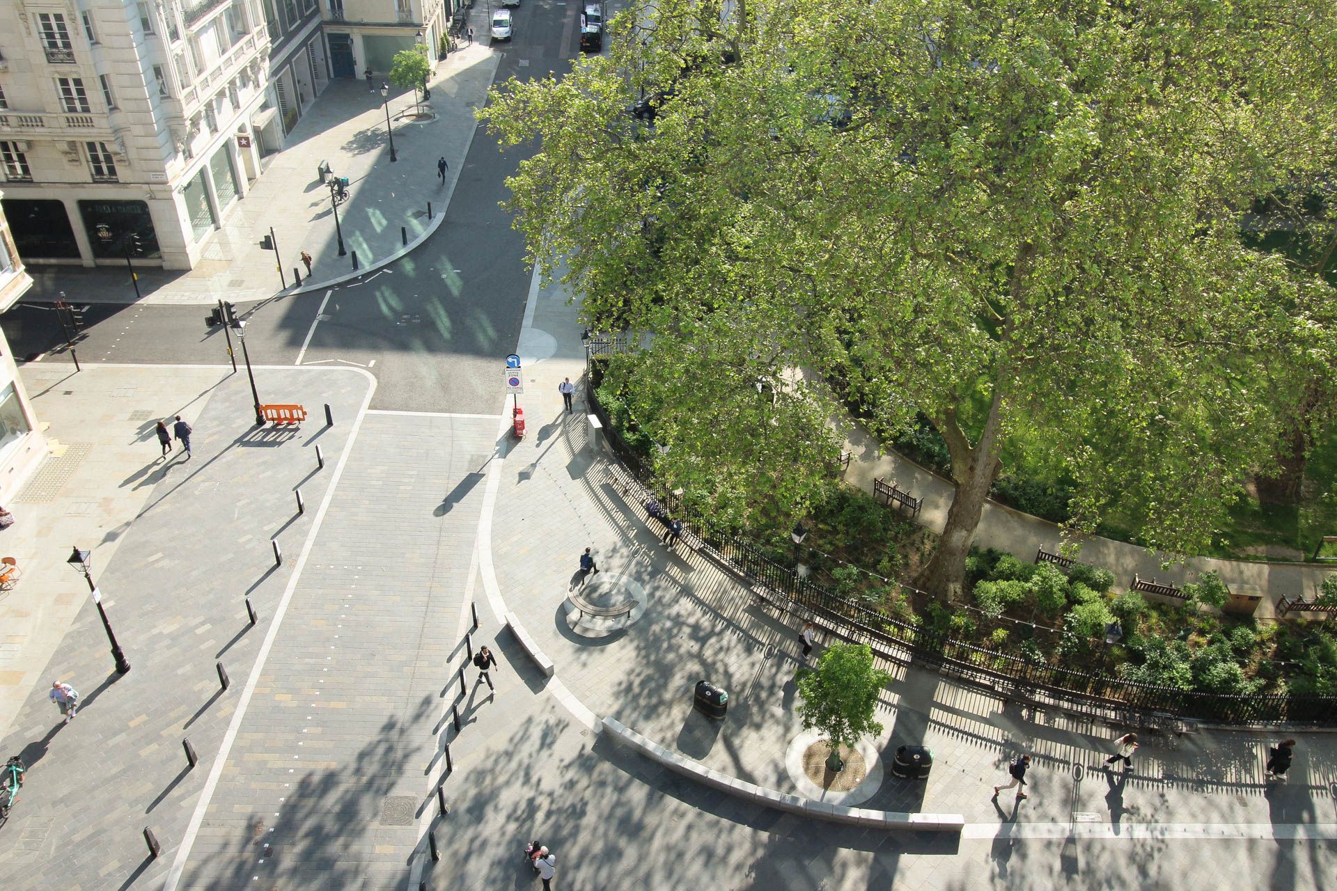 Photograph of the corner of Hanover Square taken from above with green bushes, trees and people walking on the pavement around it.