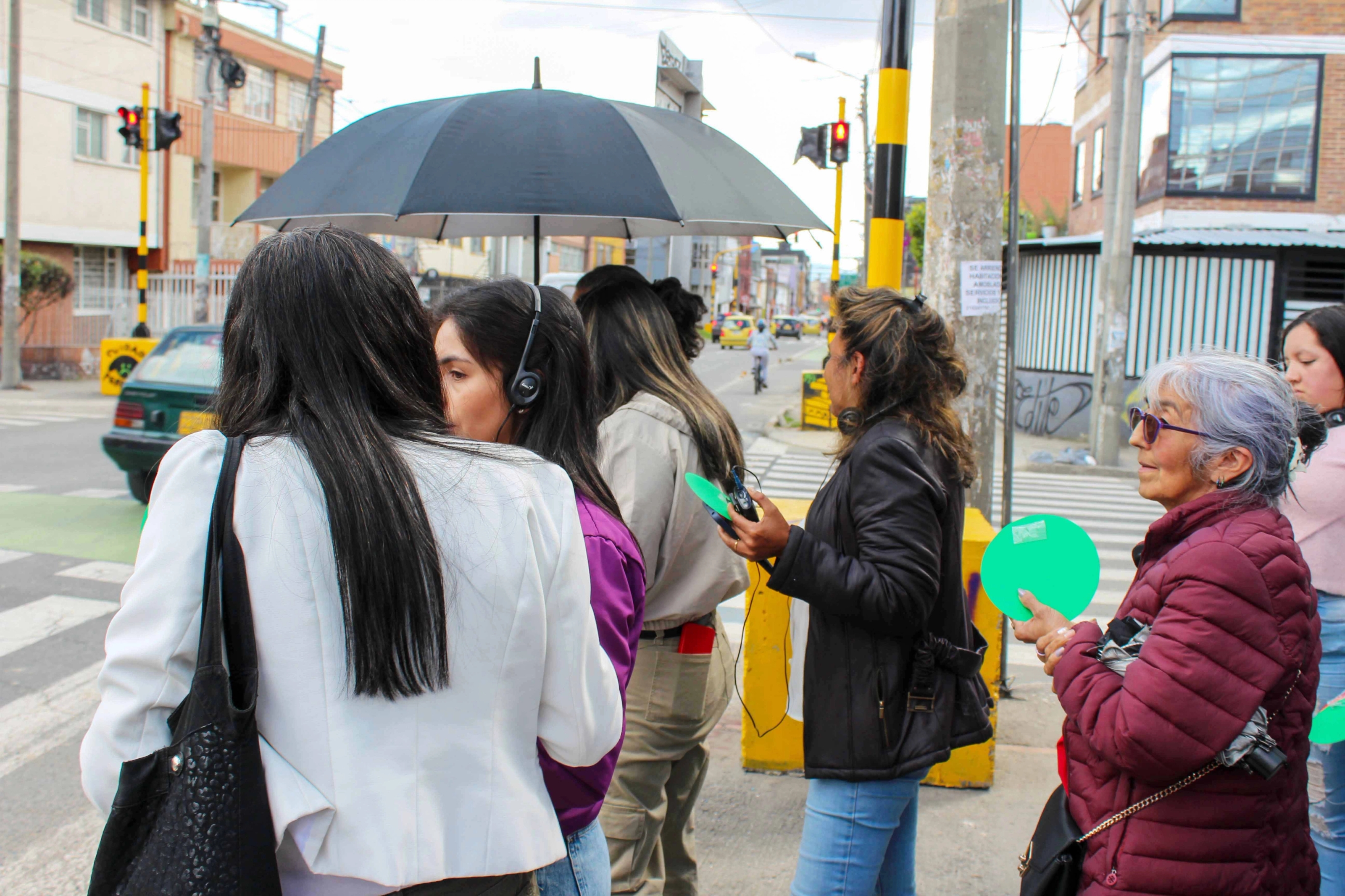 A group of people holding green paper circles waits at a pedestrian crossing.