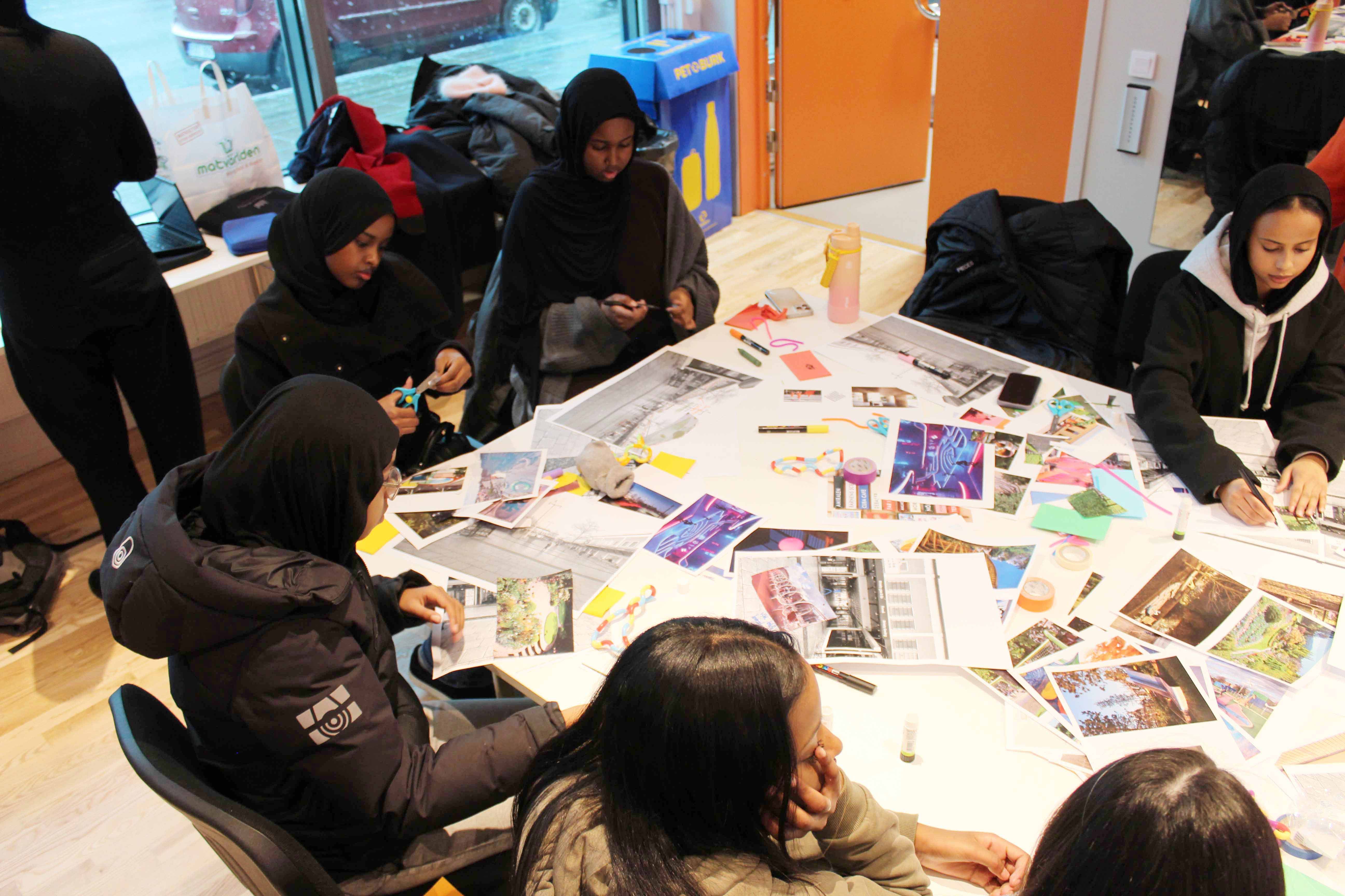 A group of young people sit around a table covered in drawings, images and photographs as they cut these out to create collages.