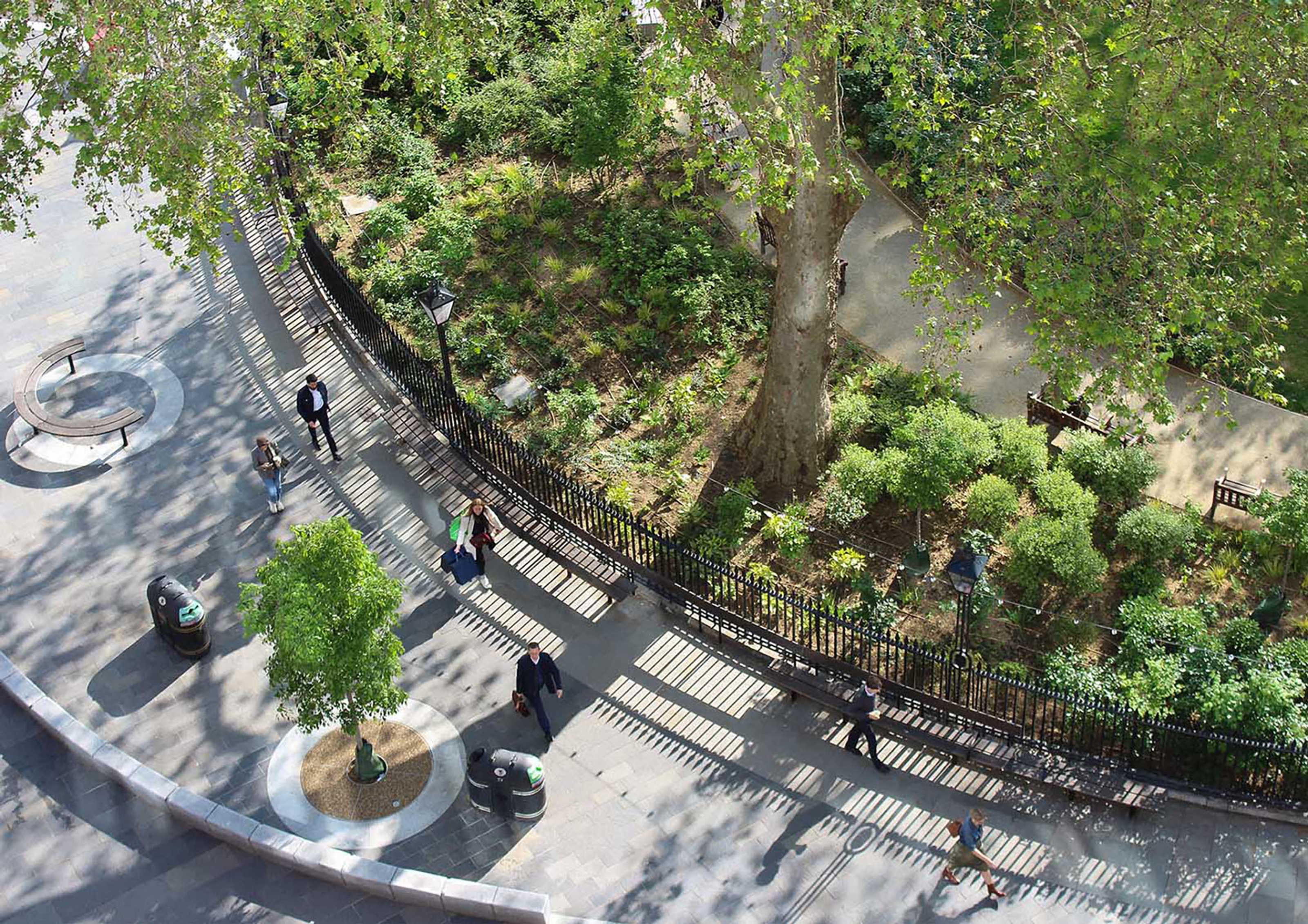 Photograph of the edge of Hanover Square taken from above with green bushes and trees and people walking on the pavement around it.