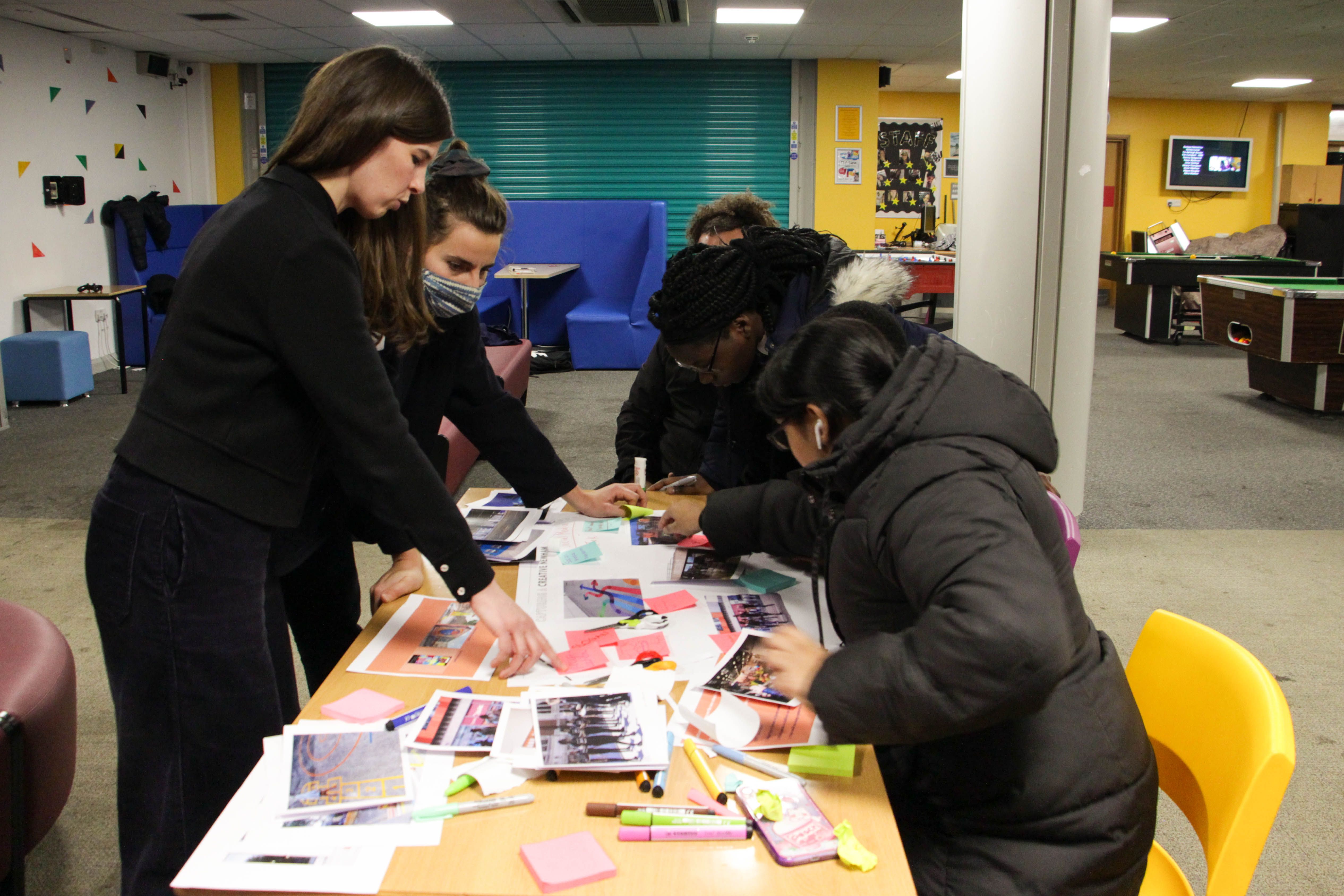 Children and young people conducting a collaging activity with two workshop facilitators watching over the exercise.