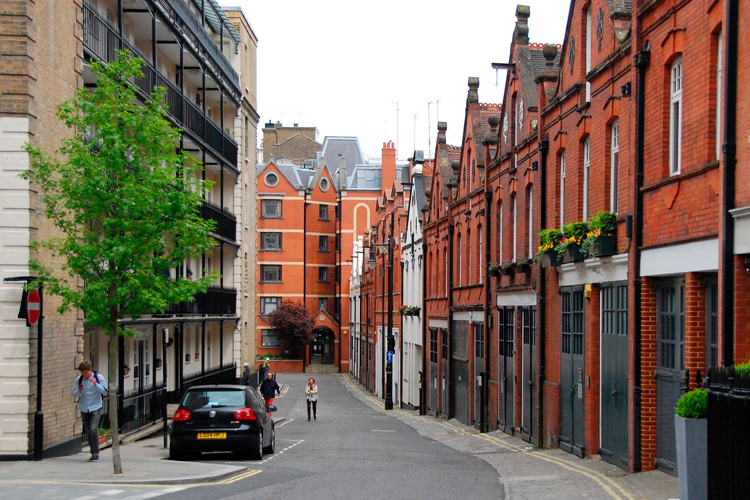 A quiet street lined with predominantly red brick buildings on the right hand side.