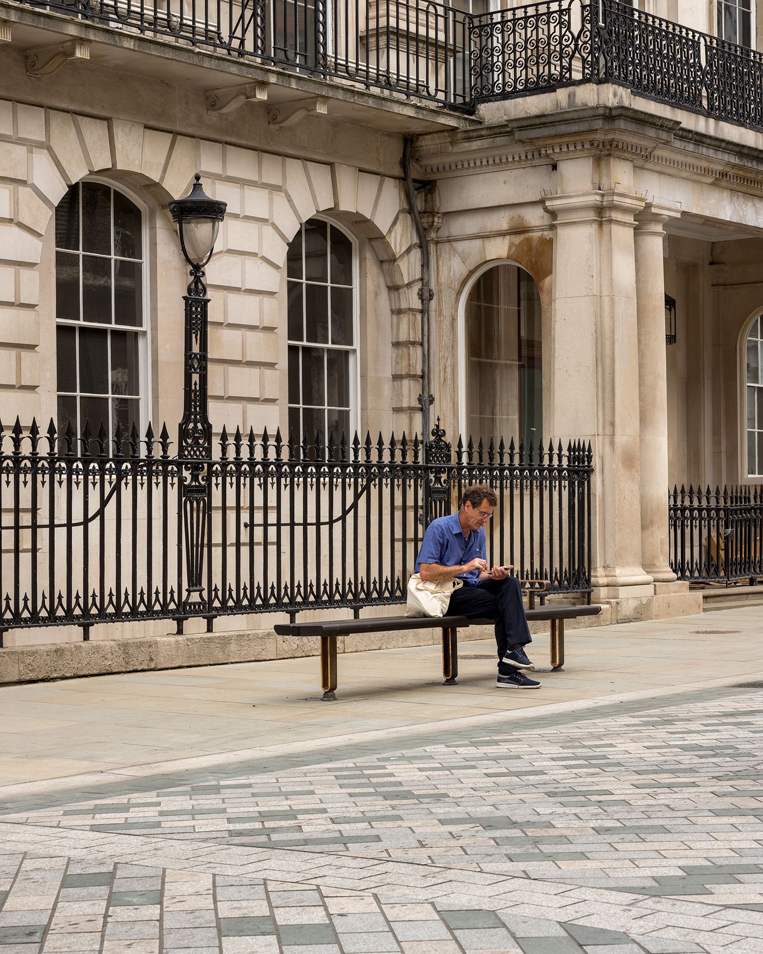 Man sitting on bench infront of building with black railling.