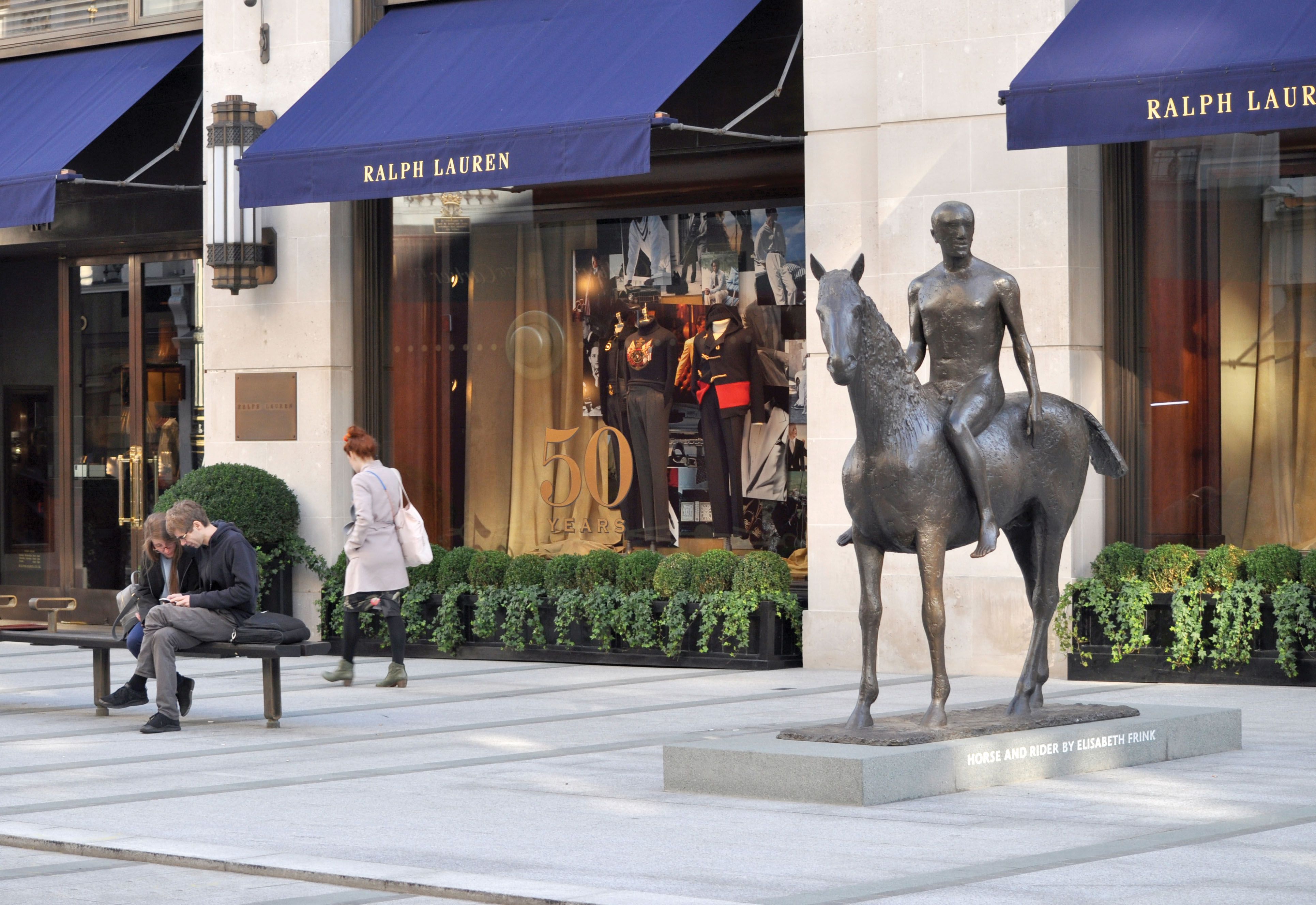 A bronze statue of a person on a horse in front of a Ralph Lauren shop.