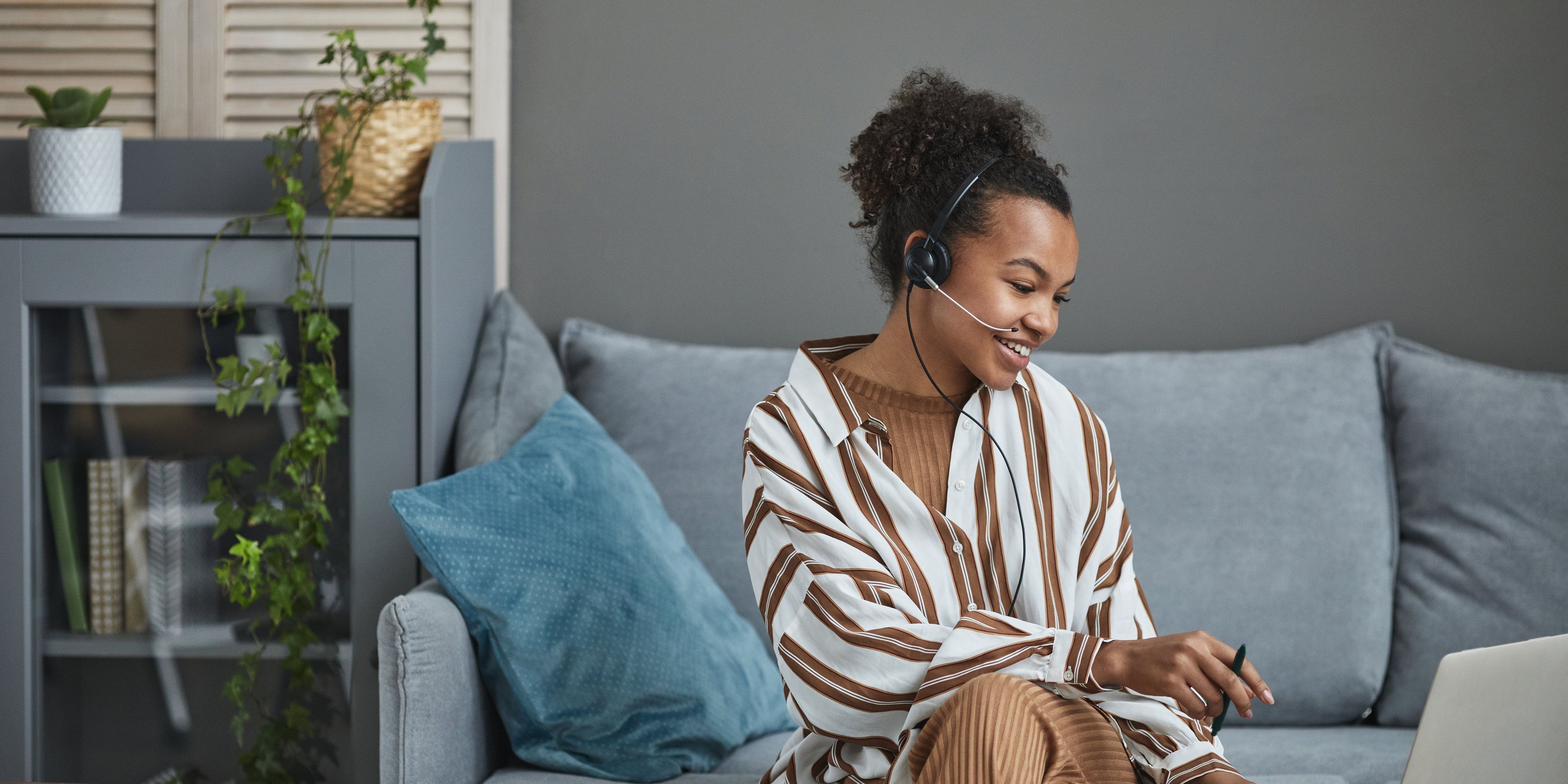a woman is sitting on a couch using a laptop and a headset .