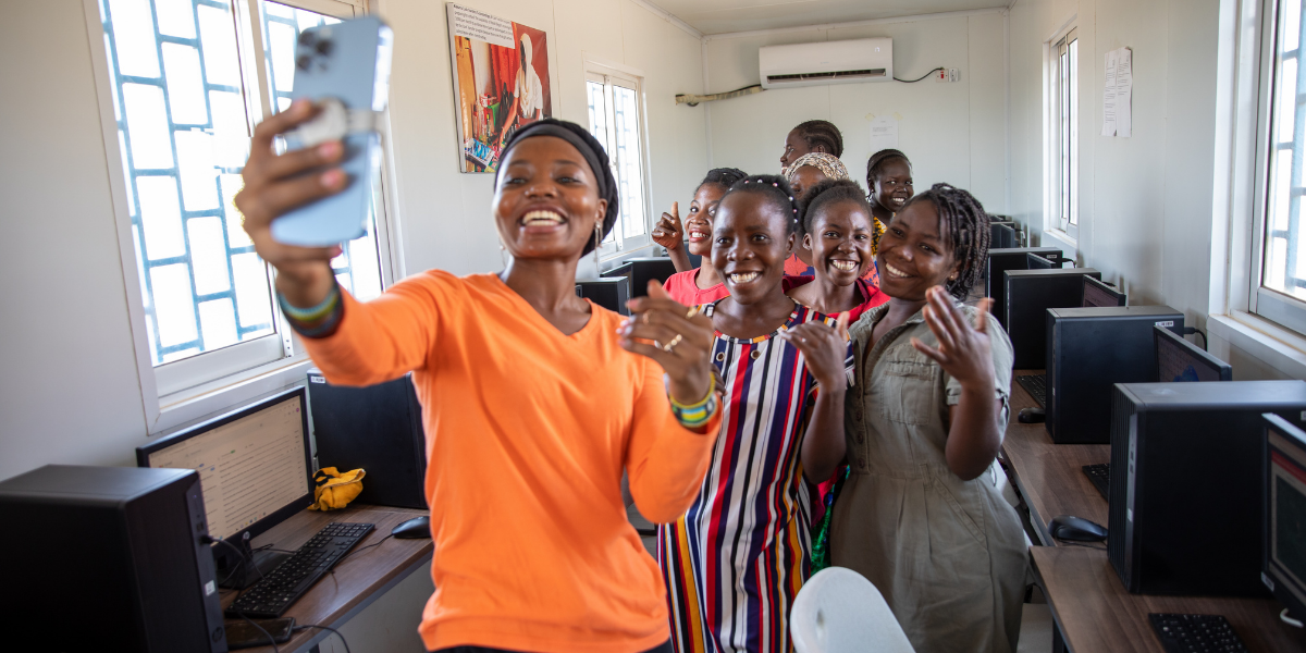 a woman taking a selfie with a group of children in front of a sign that says unhcr