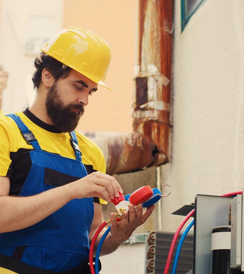 HVAC technician servicing an outdoor air conditioning unit using gauges at a residential home