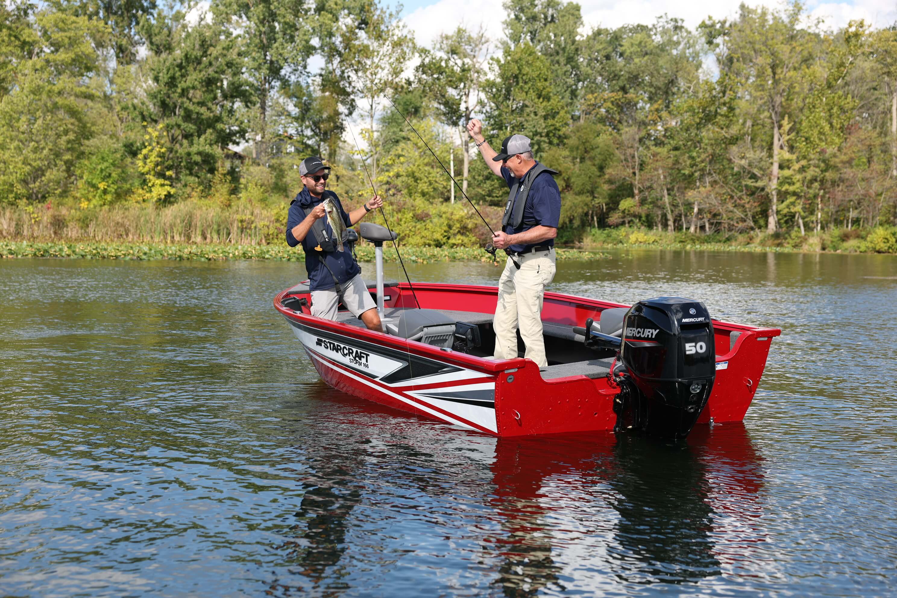 Red and white Starcraft Storm fishing boat with two anglers fishing and an outboard on the transom, on calm water near the shore