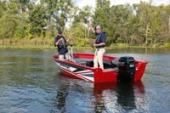 Red and white Starcraft Storm fishing boat with two anglers fishing and an outboard on the transom, on calm water near the shore