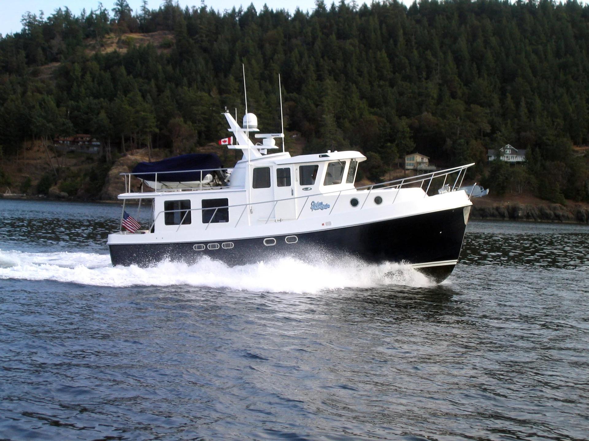 American Tug 435 with navy hull cruising along a wooded shoreline