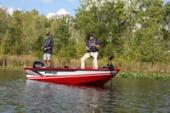Red Starcraft Storm aluminium fishing boat with two anglers standing on the deck on a calm lake with trees behind