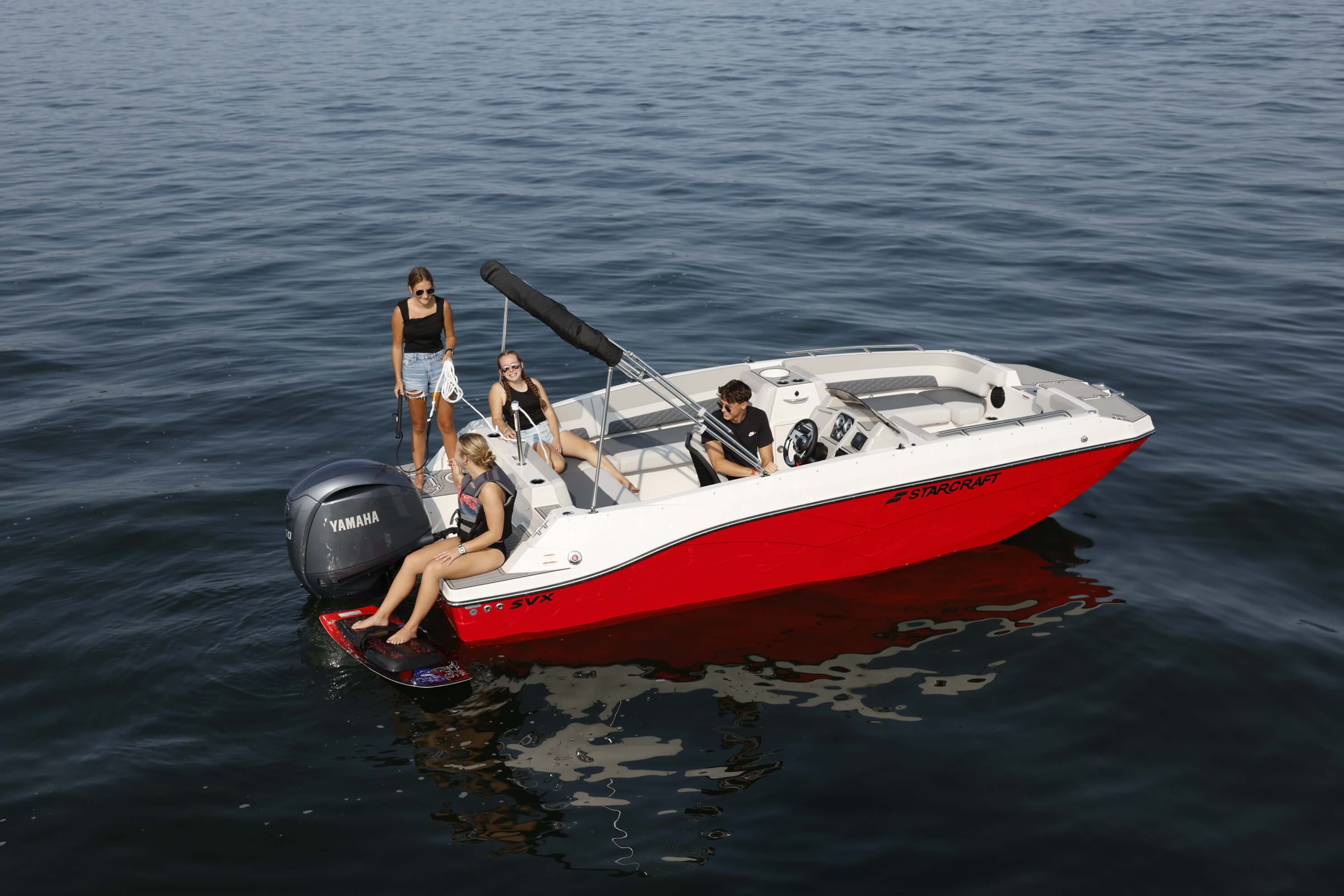 Aerial view of a red and white Starcraft SVX 191 OB deck boat with a black bimini top and outboard motor, carrying passengers on open water