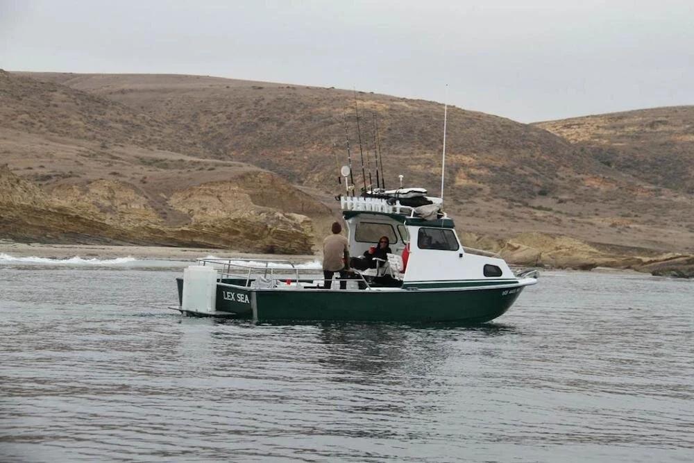Green-hulled Anderson 26 pilothouse with twin outboards and fishing rods near a beach