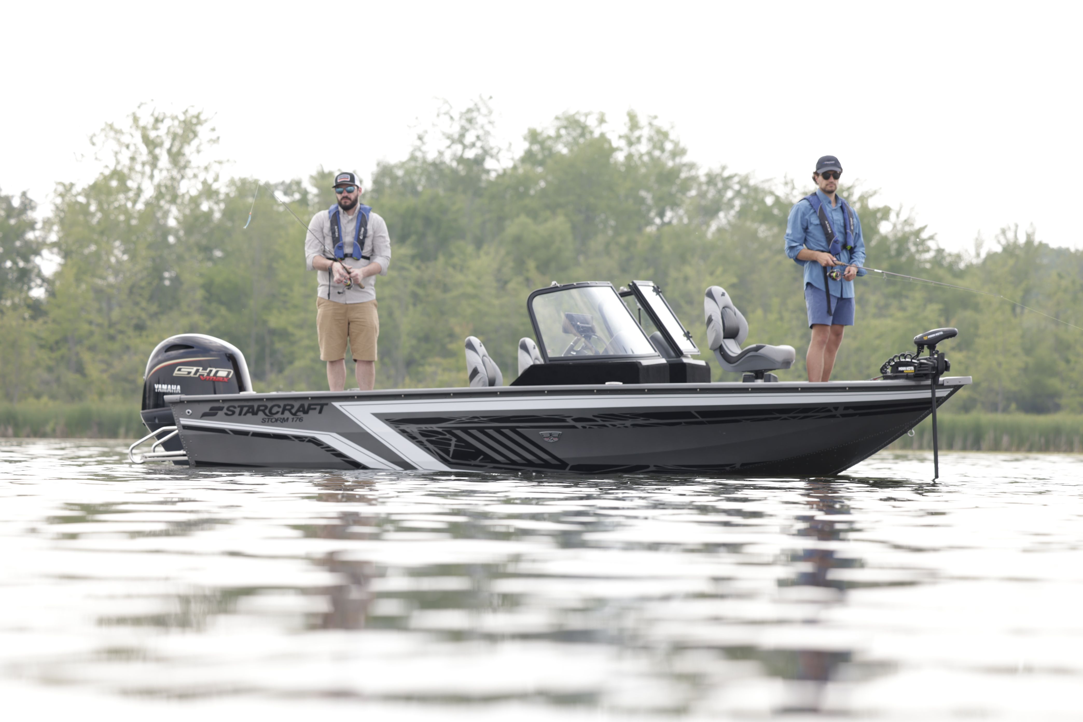 Black and grey Starcraft Storm fishing boat with two anglers casting, an outboard on the transom and trees along the bank