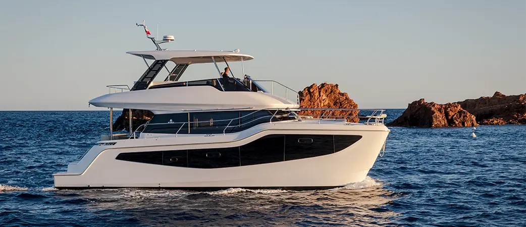 Aquila 46 Yacht flybridge power catamaran at sea beside red coastal rocks