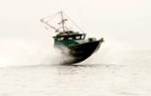Dark-green Anderson 31 commercial fishing boat launching through spray at speed