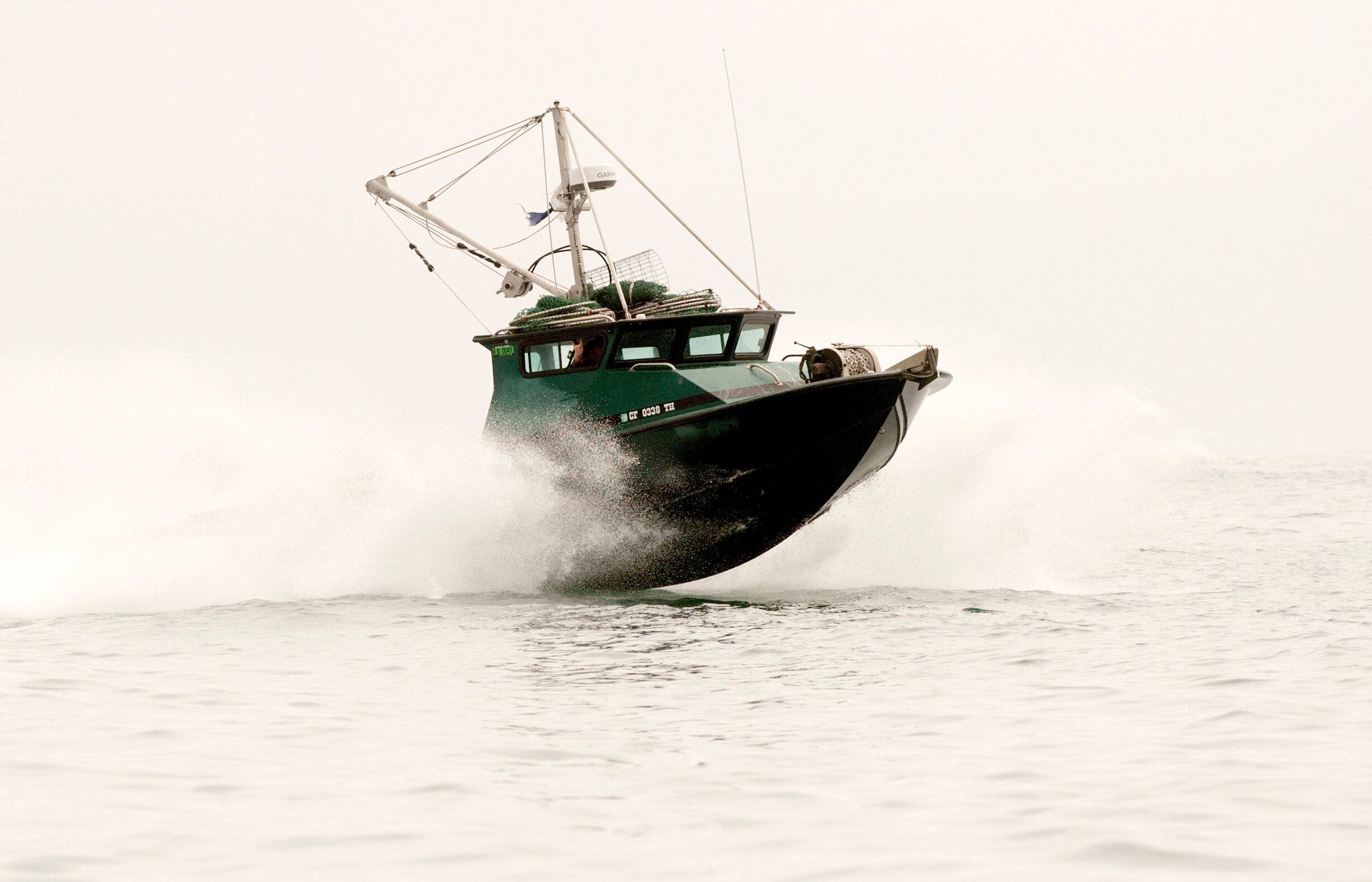 Dark-green Anderson 31 commercial fishing boat launching through spray at speed