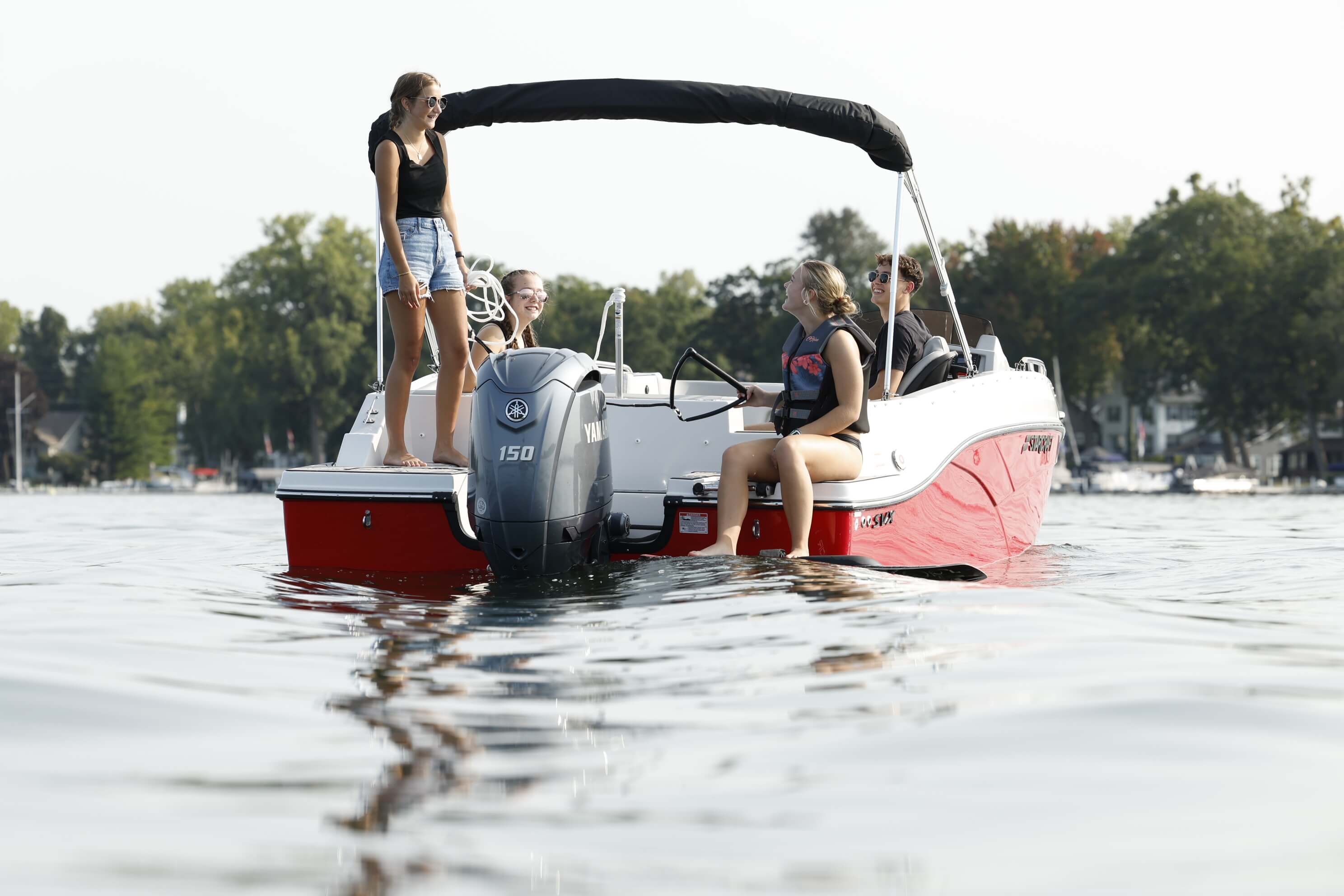 Starcraft SVX 191 OB deck boat with a black bimini top, a passenger standing at the stern and an outboard motor on calm lake water