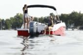 Starcraft SVX 191 OB deck boat with a black bimini top, a passenger standing at the stern and an outboard motor on calm lake water