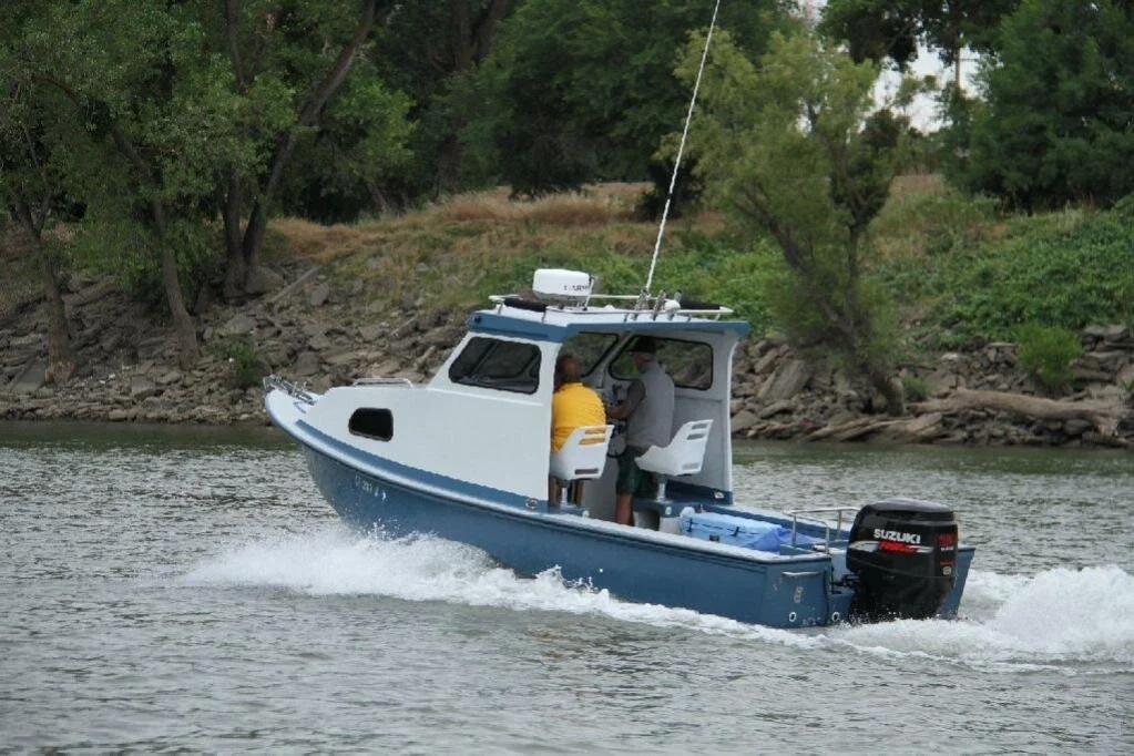 Blue-hulled Greenough 21 pilothouse with single Suzuki outboard cruising along a riverbank