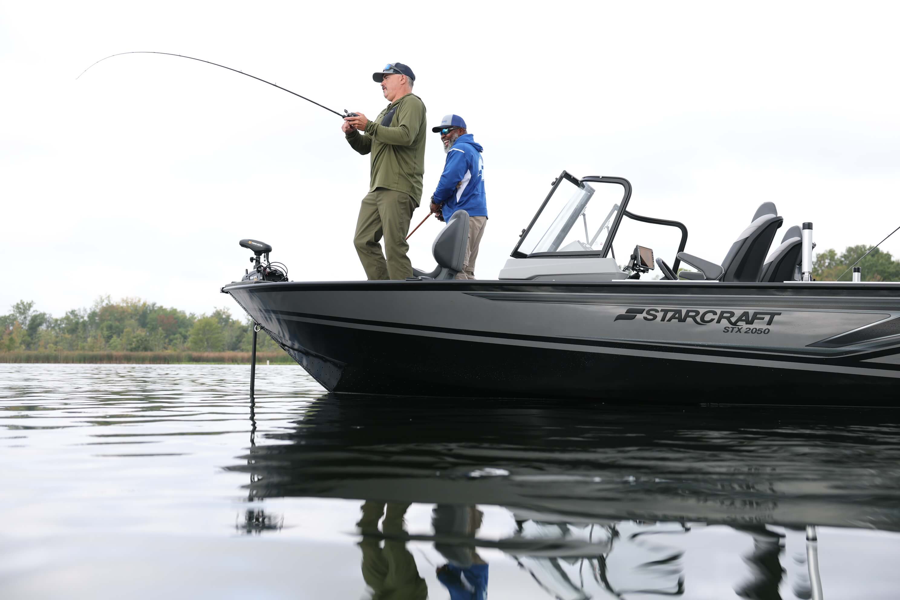 Anglers casting from the bow deck of a Starcraft STX 2050 with a windscreen and console, reflected in still water