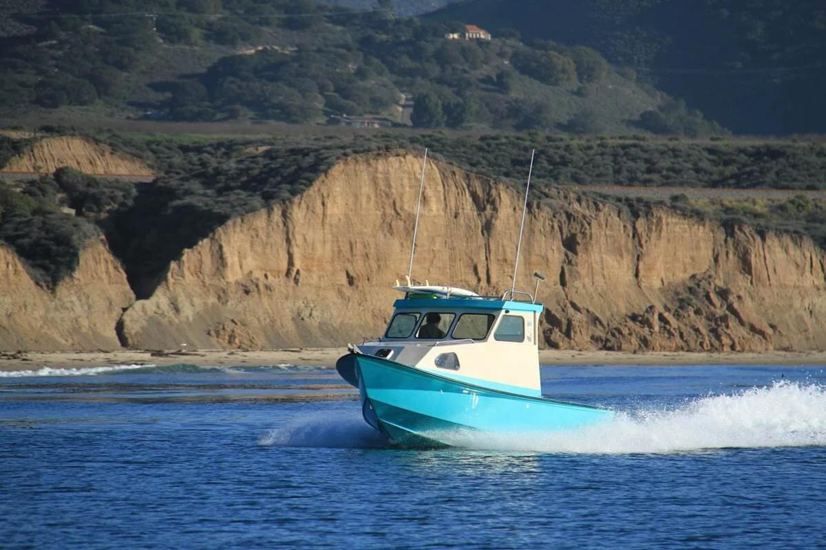 Turquoise Greenough 21 pilothouse planing past sandstone coastal cliffs