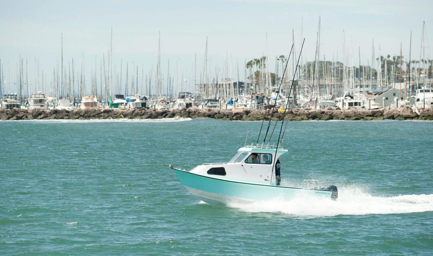 Greenough 21 pilothouse rigged with fishing rods heading out from a marina breakwater