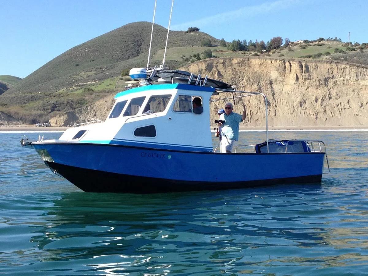 Blue-hulled Anderson 26 pilothouse at anchor below coastal bluffs with crew on deck