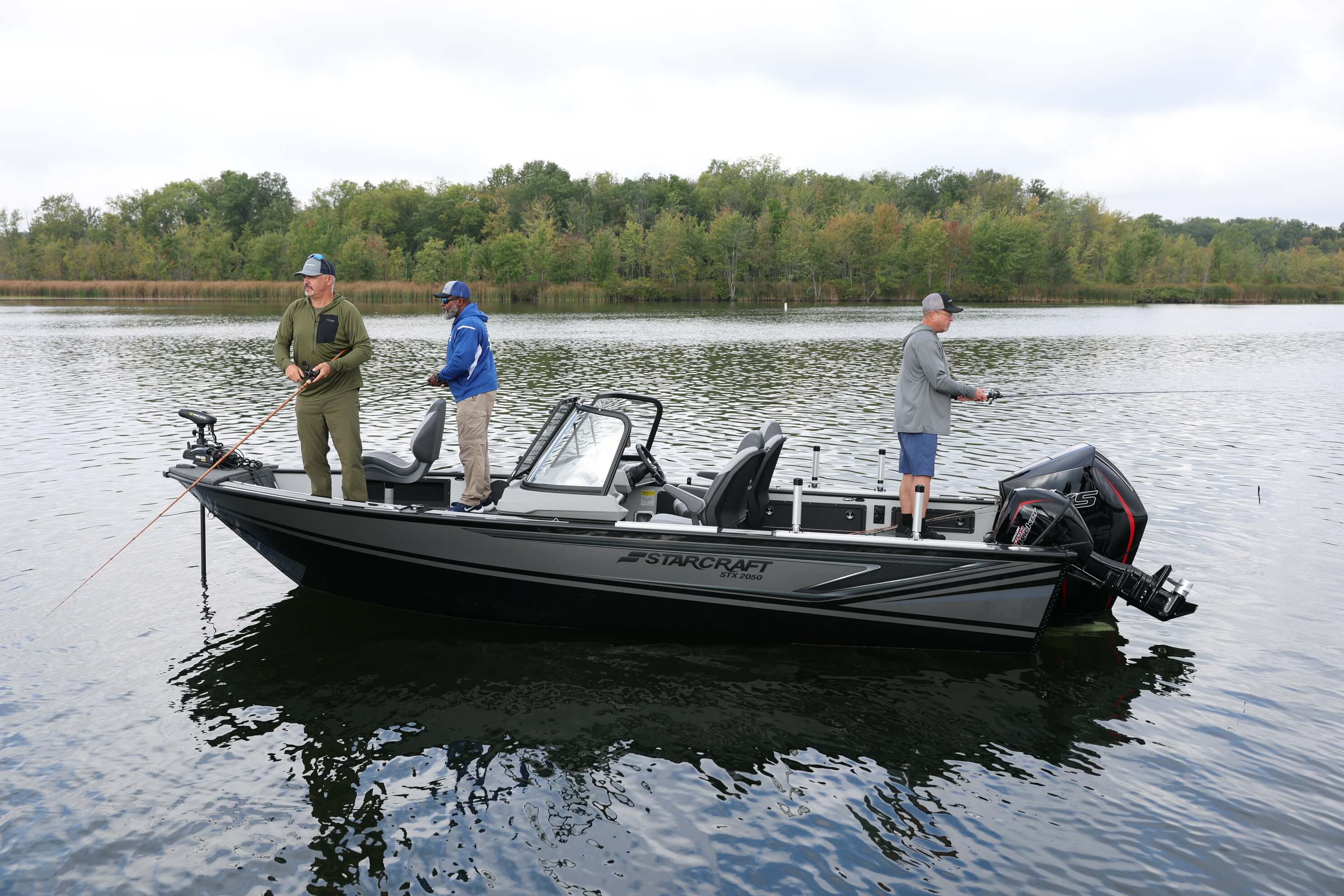 Three anglers fishing from a dark Starcraft STX 2050 with a bow-mounted trolling motor and outboard on a calm lake