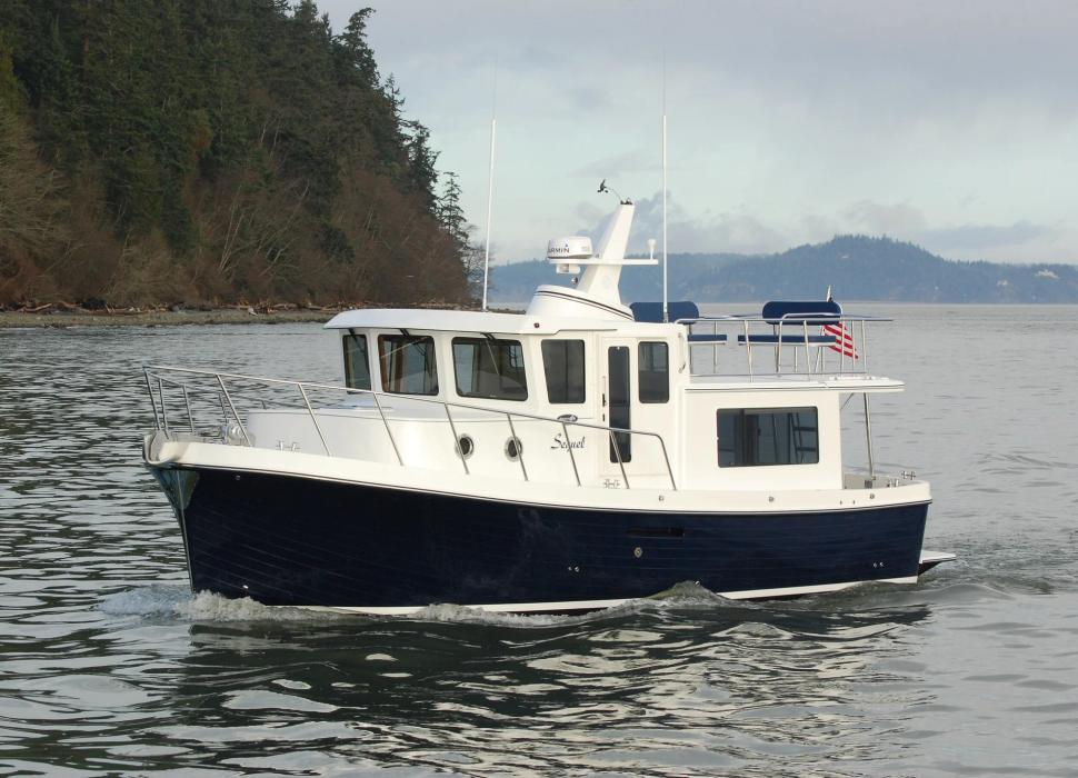 American Tug 365 with dark blue hull cruising along a wooded shoreline