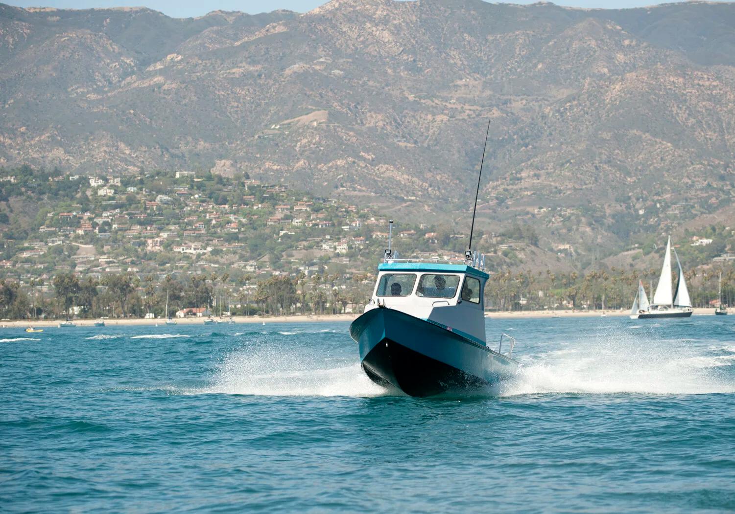 Greenough 17 pilothouse planing head-on towards the camera with coastal mountains behind