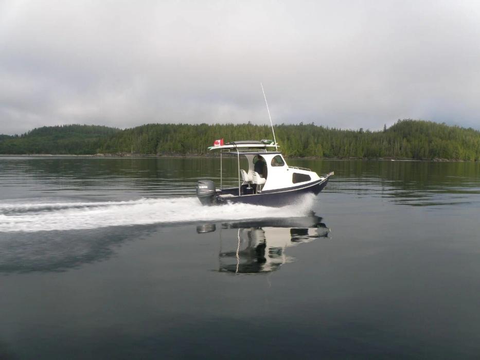 Greenough 17 pilothouse skiff with outboard cruising on calm water along a forested shoreline