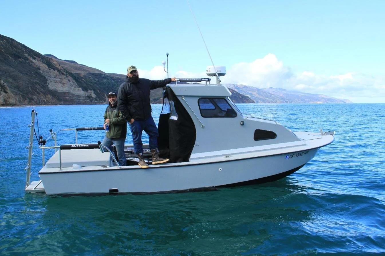Two anglers aboard a white Anderson 22 pilothouse off a rugged coastline