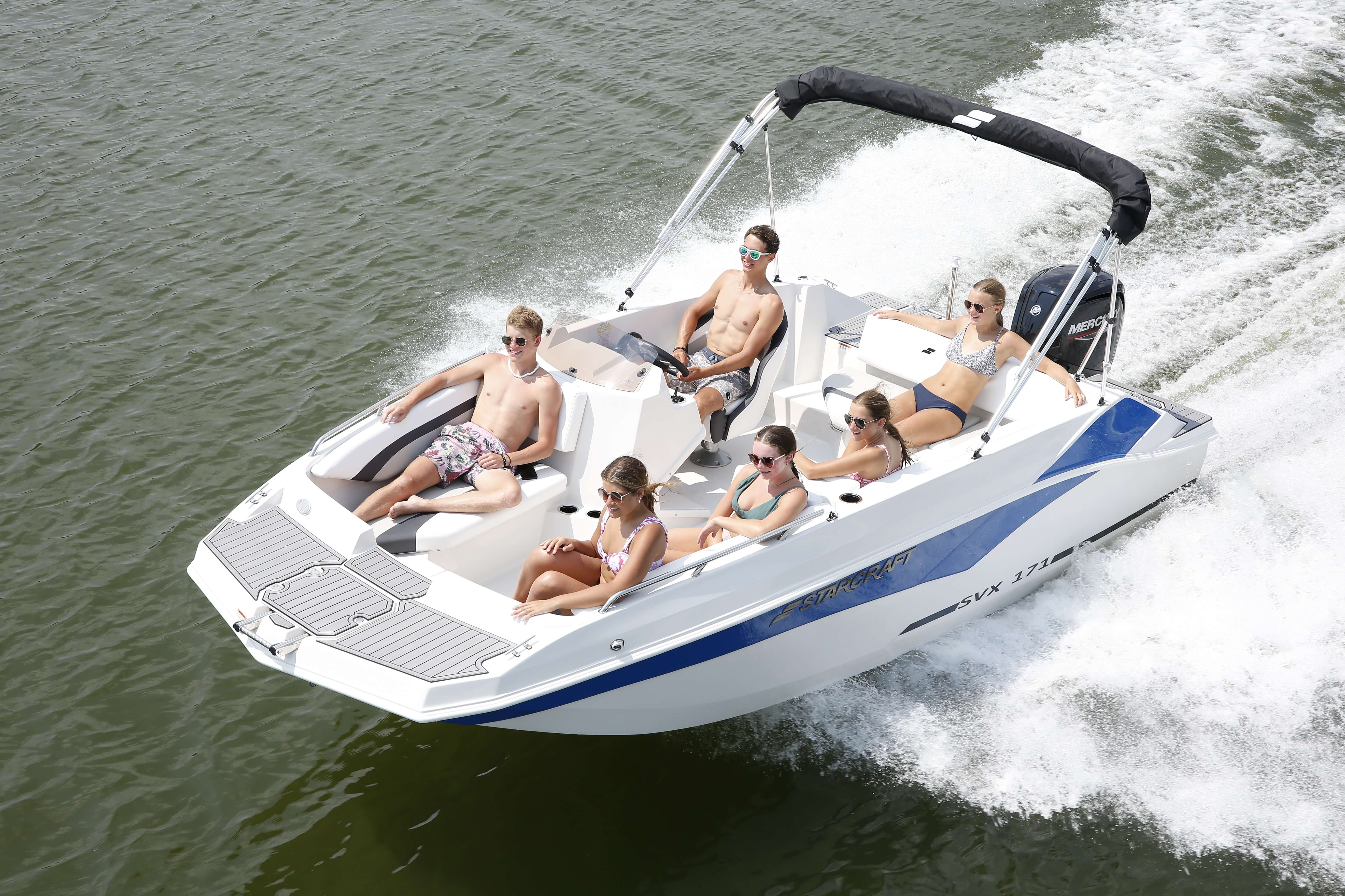 Passengers relaxing aboard a white and blue Starcraft SVX 171 OB deck boat planing across a lake under a black bimini top