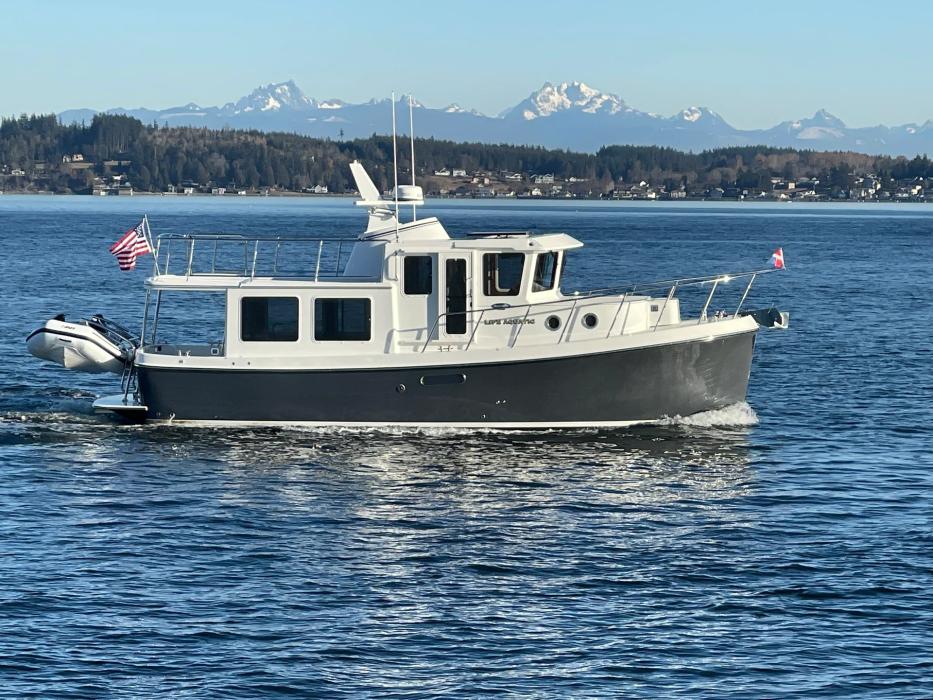 American Tug 362 pilothouse cruiser with dark hull underway, mountains behind