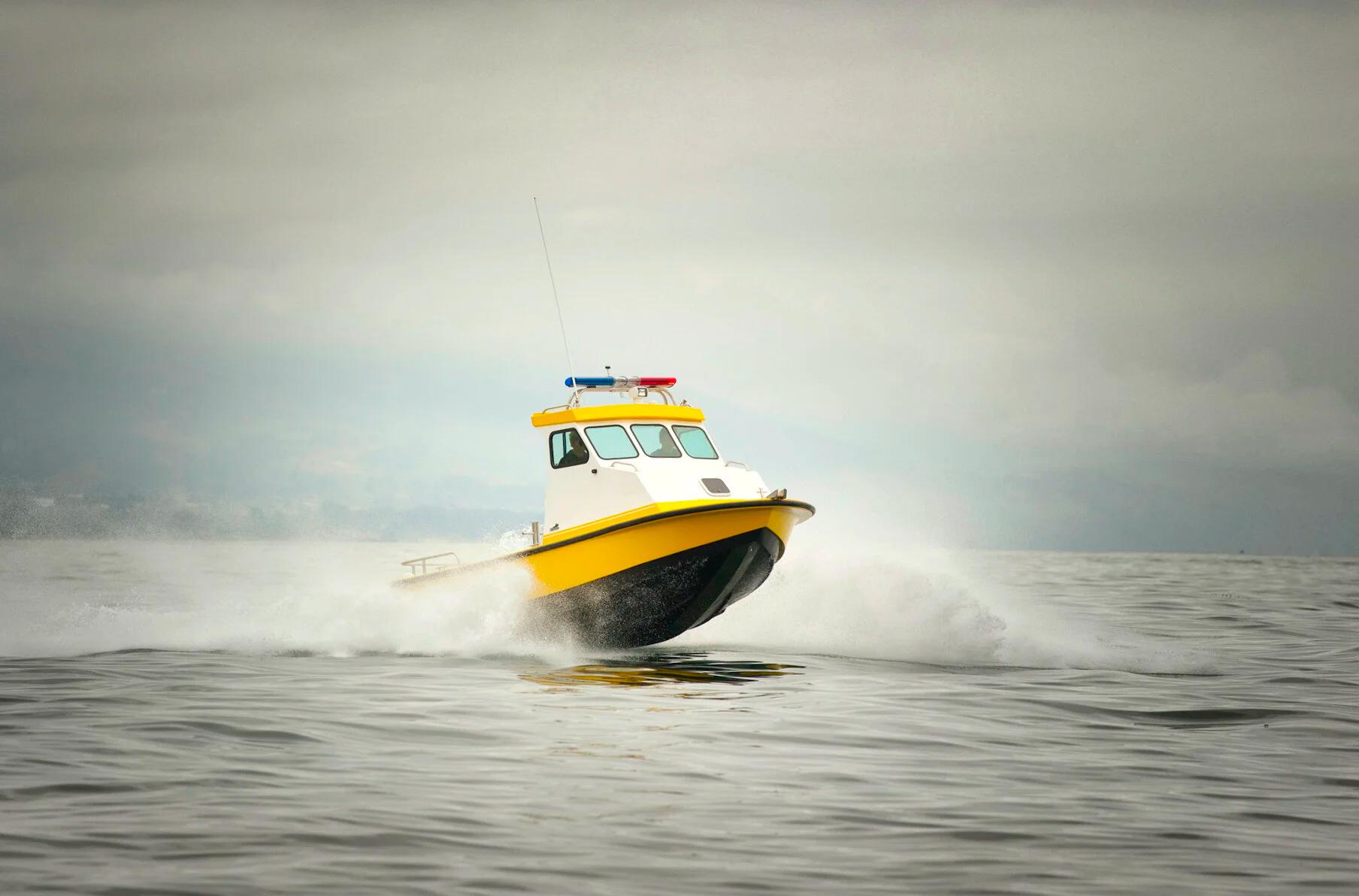 Yellow Anderson 22 patrol pilothouse with light bar running at speed through spray