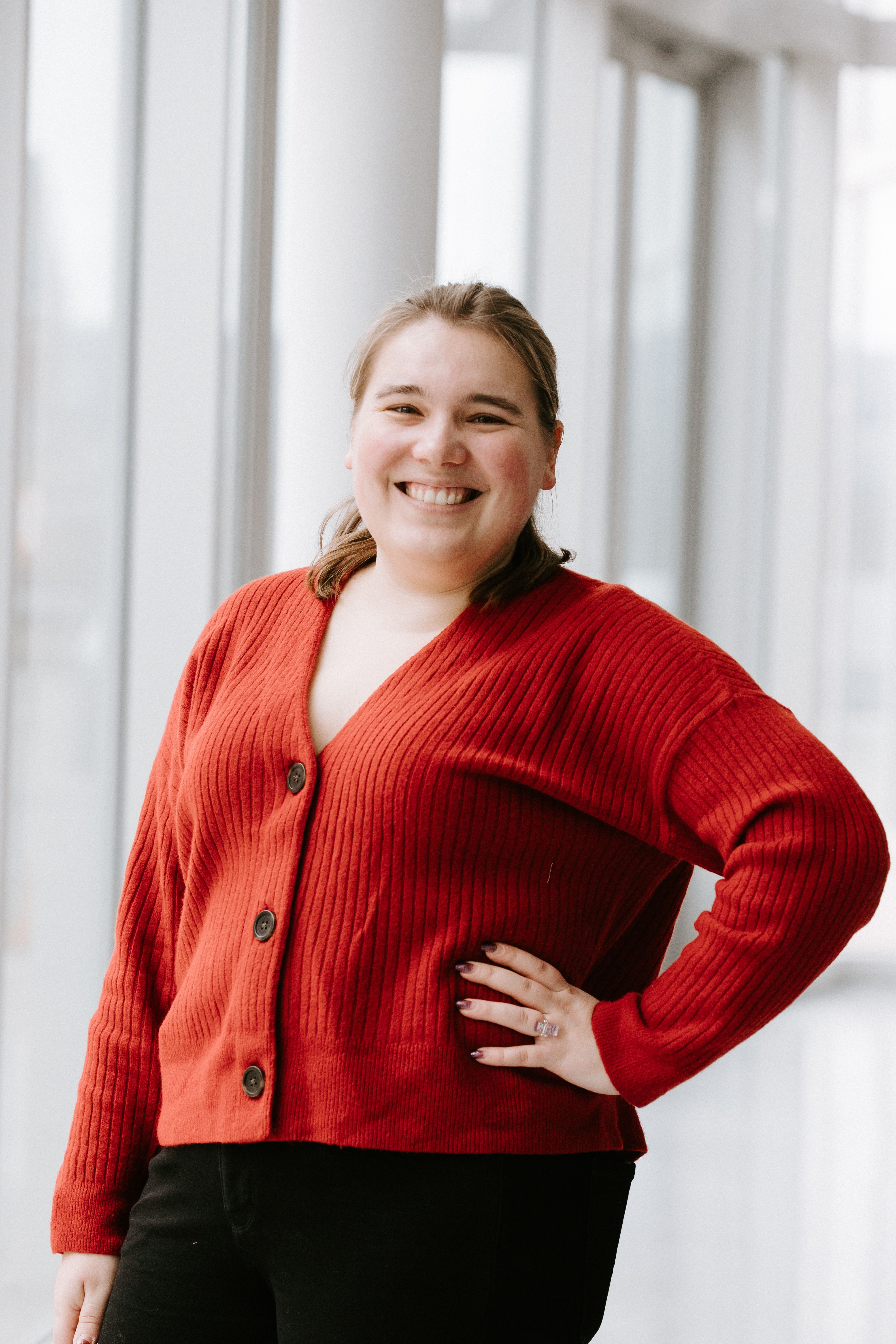 Smiling woman in a red cardigan stands with hand on hip
