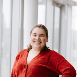 Smiling woman in a red cardigan stands with hand on hip