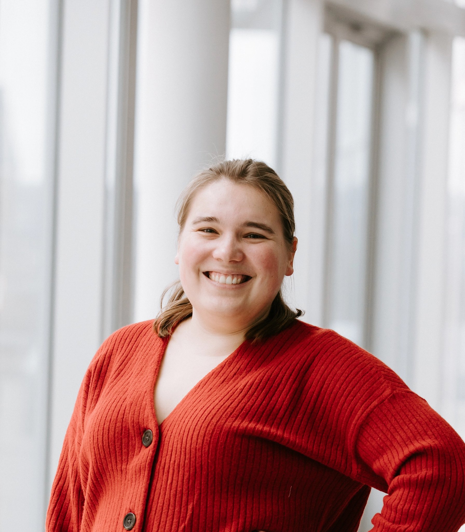 Smiling woman in a red cardigan stands with hand on hip