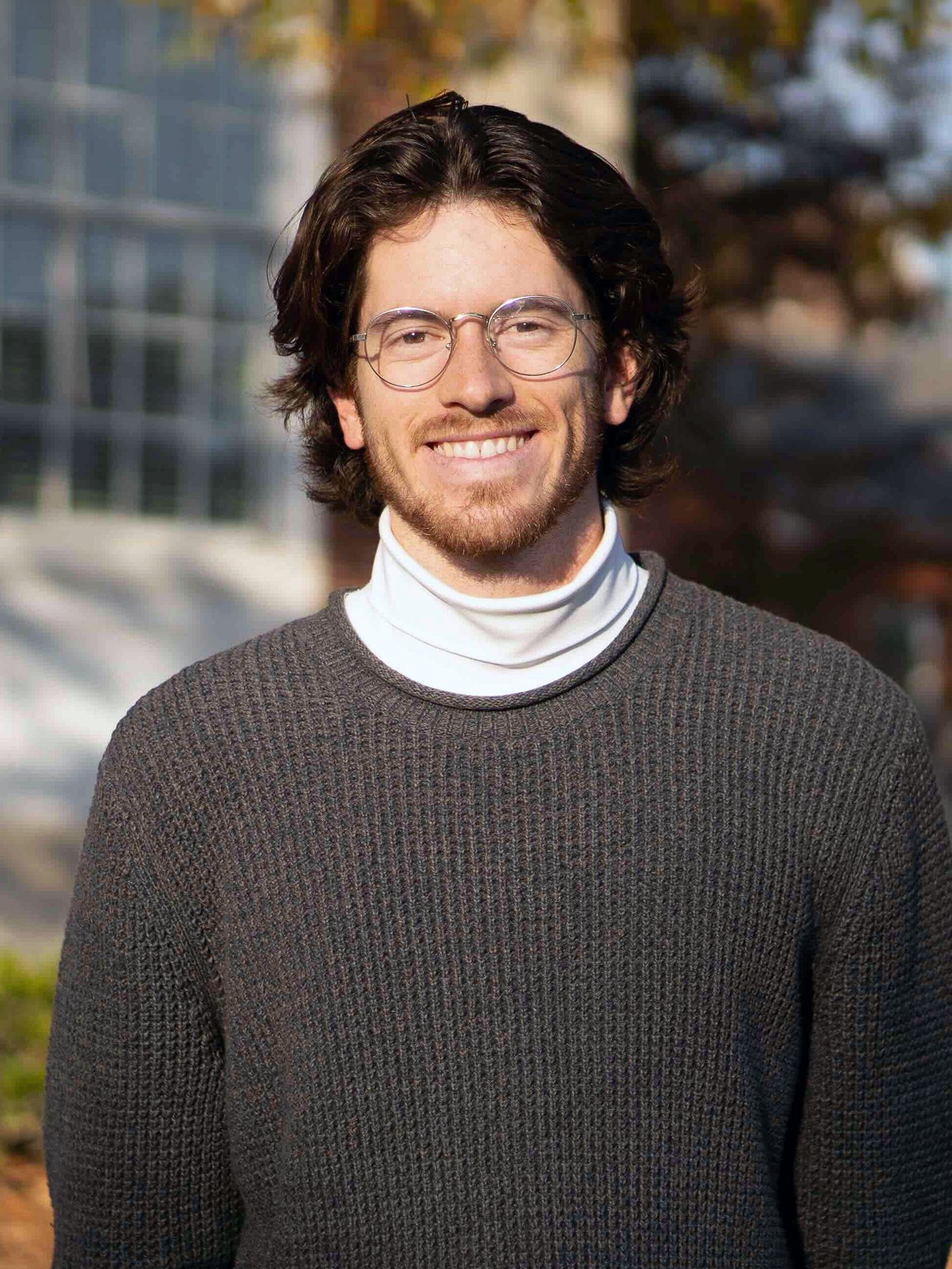 Smiling man with glasses wearing a sweater and turtleneck