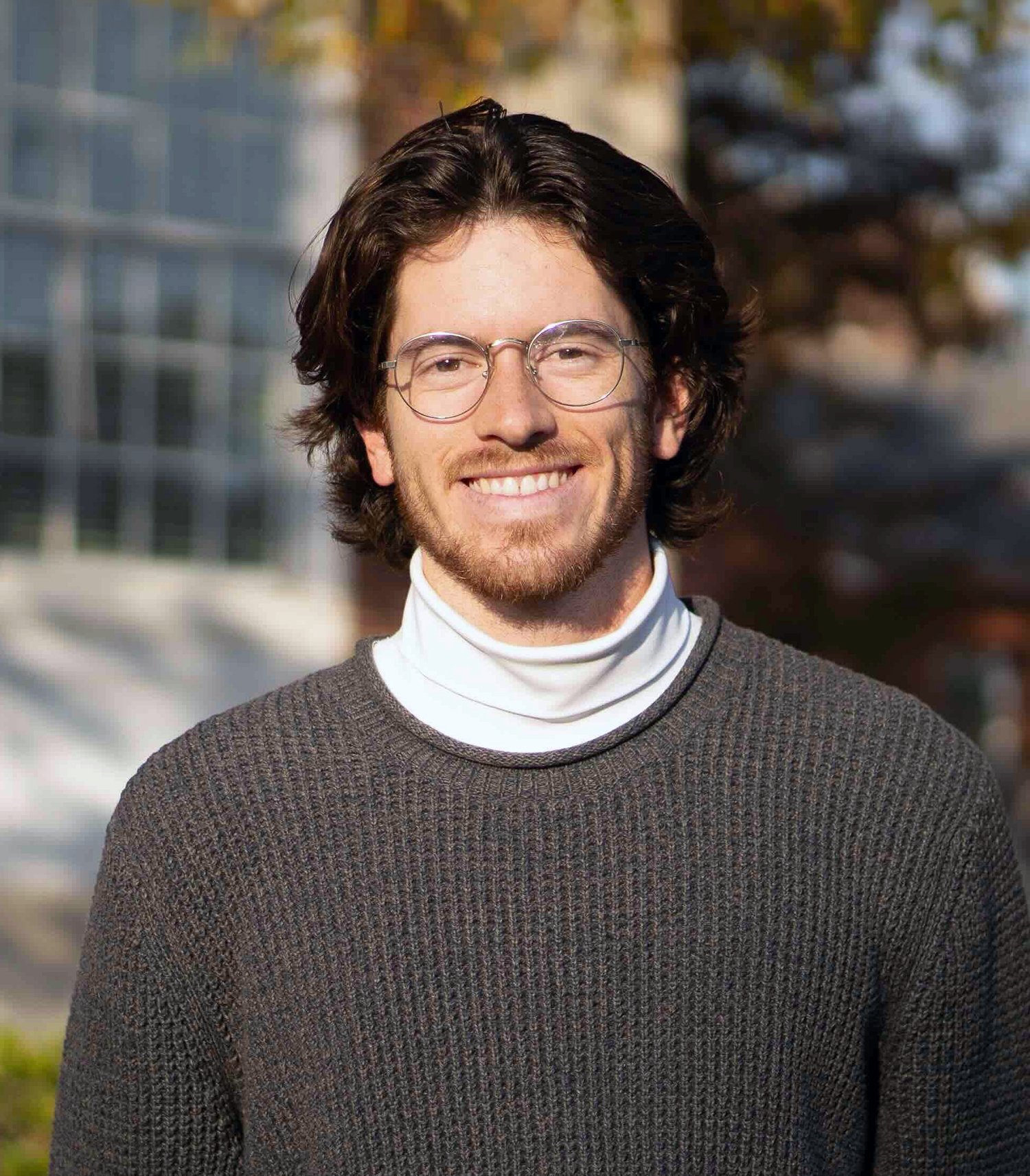 Smiling man with glasses wearing a sweater and turtleneck